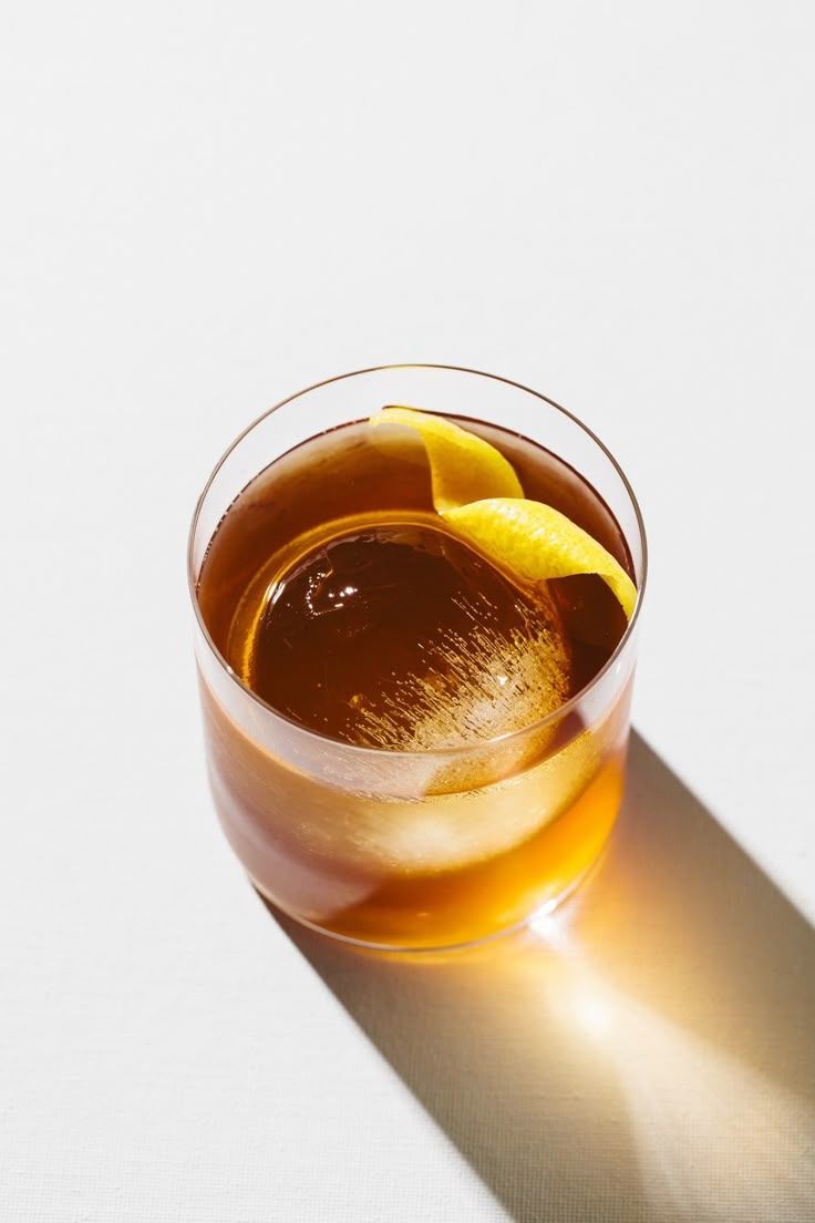 Top view of amber cocktail with lemon twist in rocks glass casting golden shadow on white.