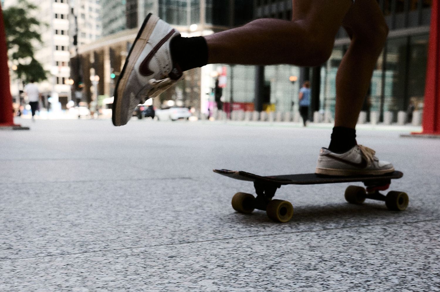 Person skateboarding on a city street, captured at ground level showing sneakers and a wooden skateboard with yellow wheels.