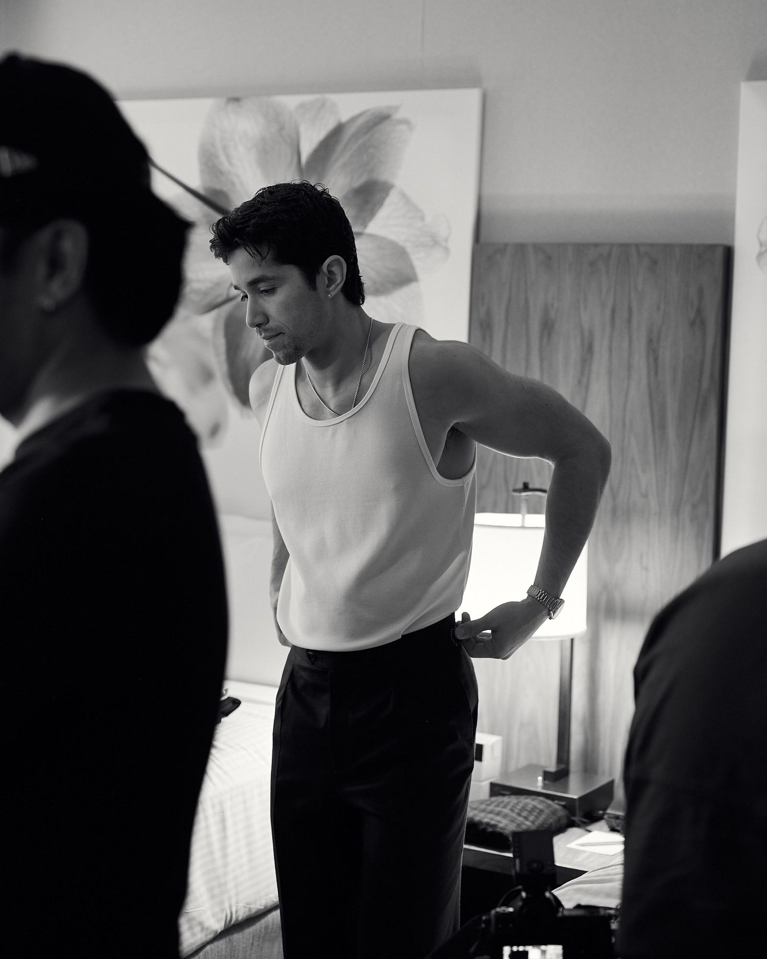 Black and white behind-the-scenes photo of a male model in a white tank top adjusting his outfit.