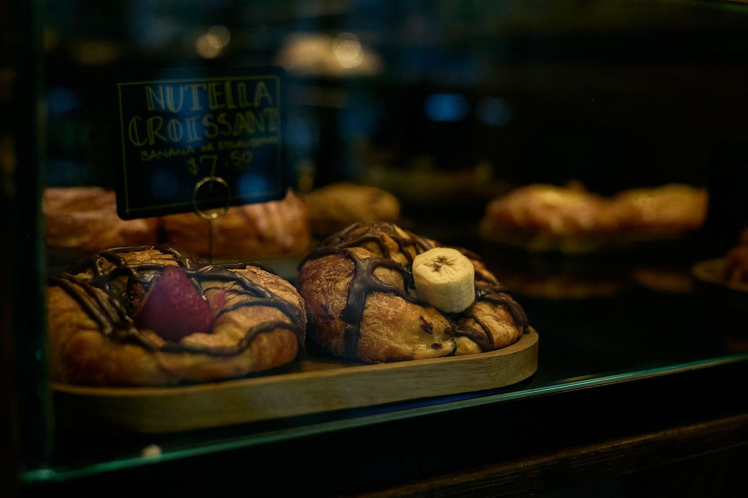 Nutella croissants with chocolate drizzle displayed in a bakery glass case under warm lighting.