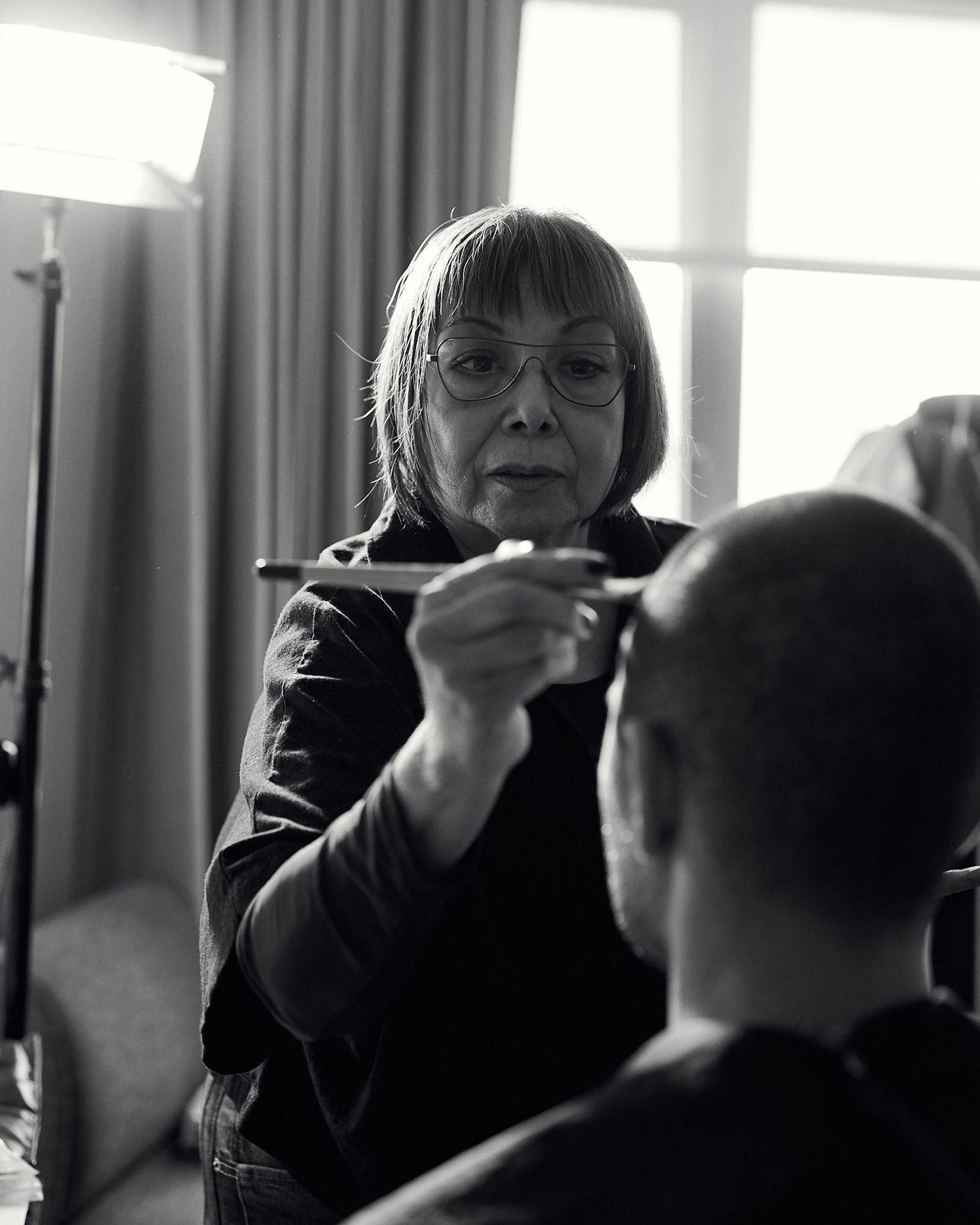 Black and white photo of a woman applying makeup to a bald man in a professional studio setting.