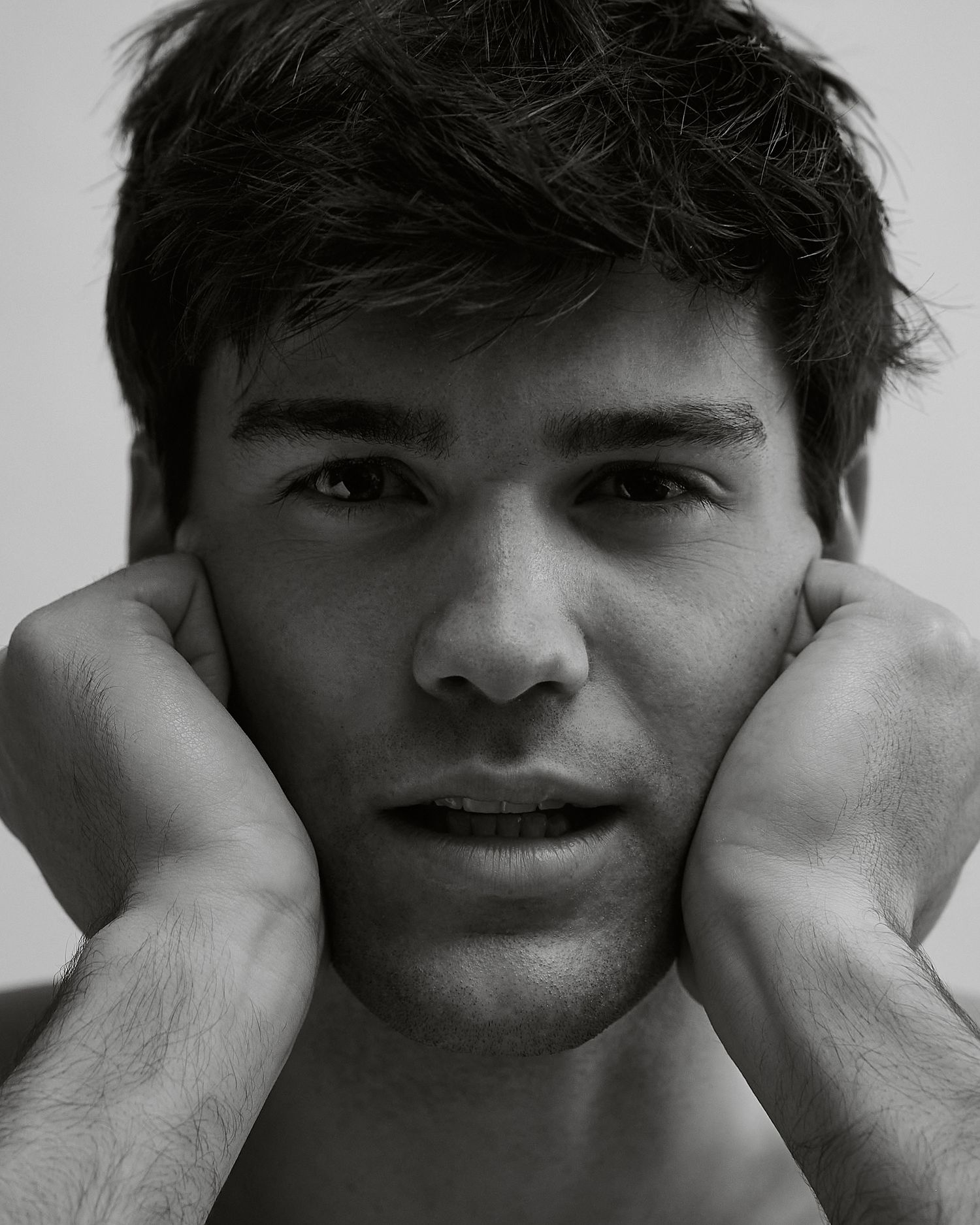 Black and white close-up portrait of a young man resting his face in both hands.