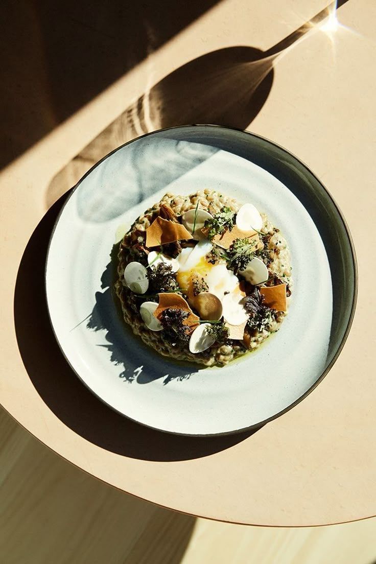 Gourmet mushroom risotto with roasted squash, fresh herbs, and cream dollops served in a ceramic bowl in natural sunlight.