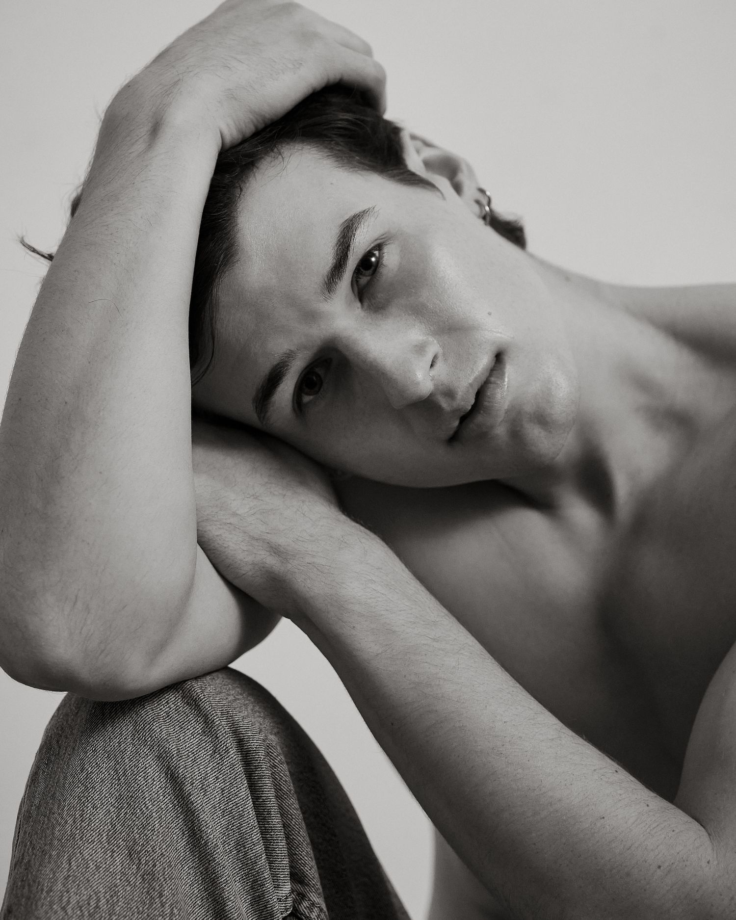 Black and white artistic portrait of shirtless young man resting head on arms, soft light background.