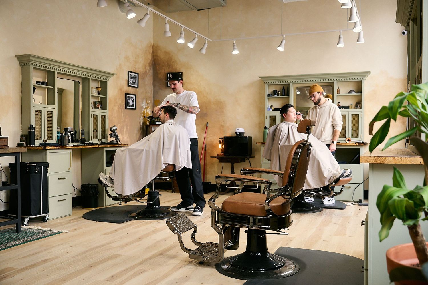 Classic barbershop interior with barbers cutting hair in vintage leather chairs, mirrors, and elegant wooden cabinetry.