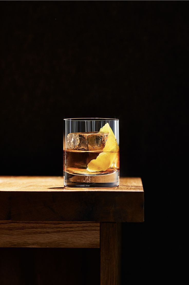 A classic Old Fashioned cocktail with ice cubes and an orange peel garnish in a rocks glass on a wooden table.
