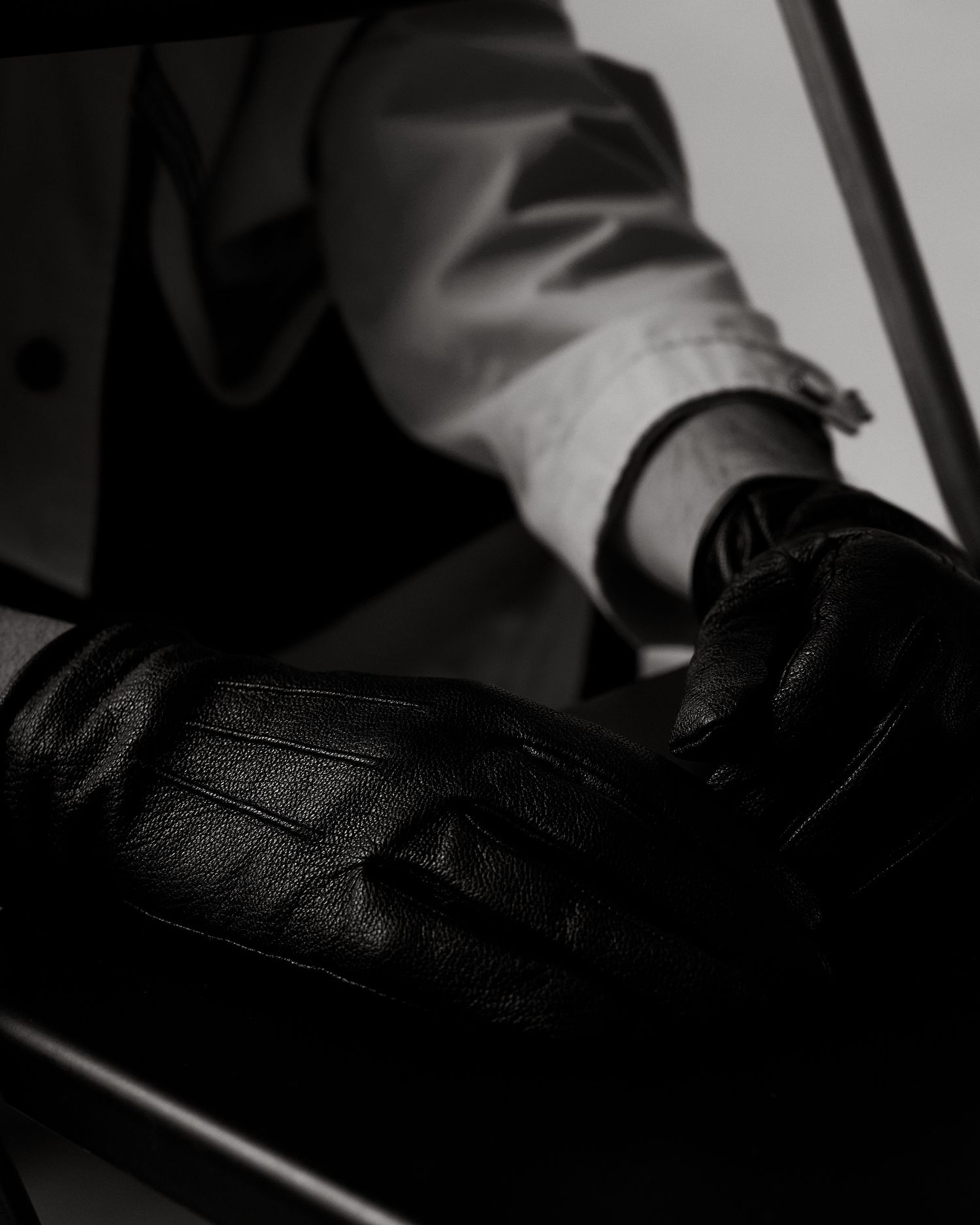 Black and white close-up of black leather gloves being worn with a white dress shirt.