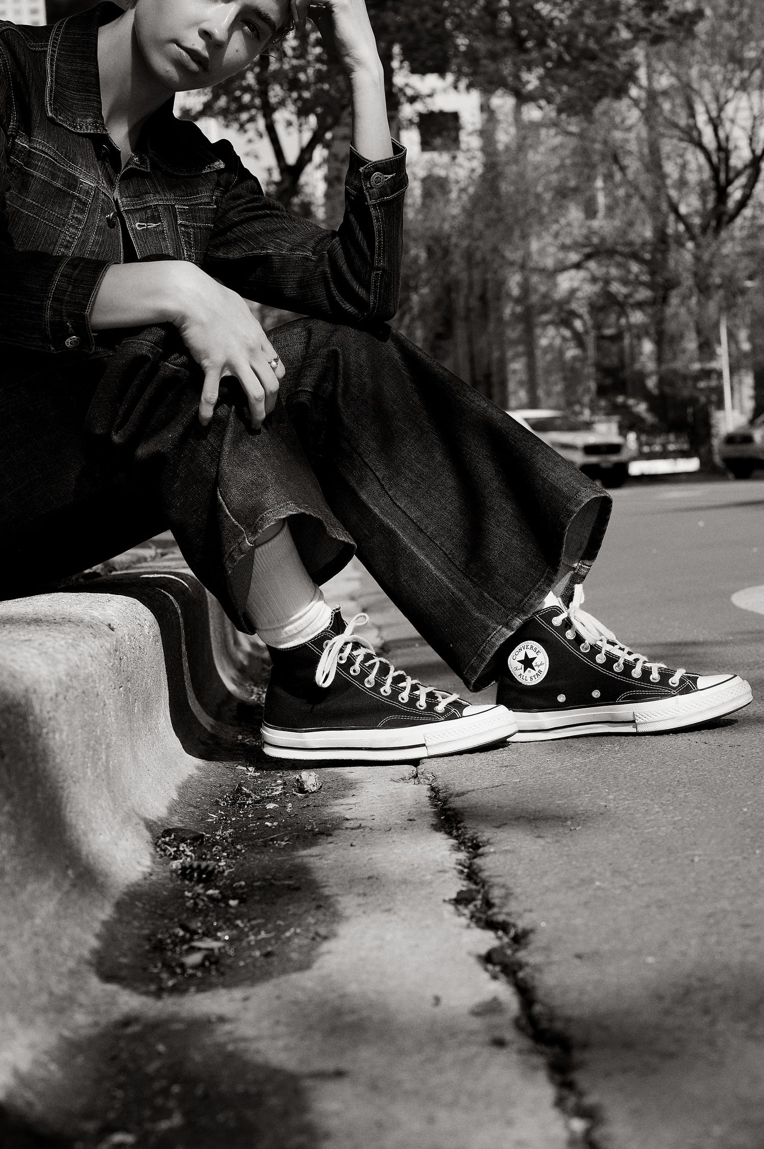 Close-up of black Converse Chuck Taylor high-top sneakers worn with wide-leg jeans on outdoor stone ledge.