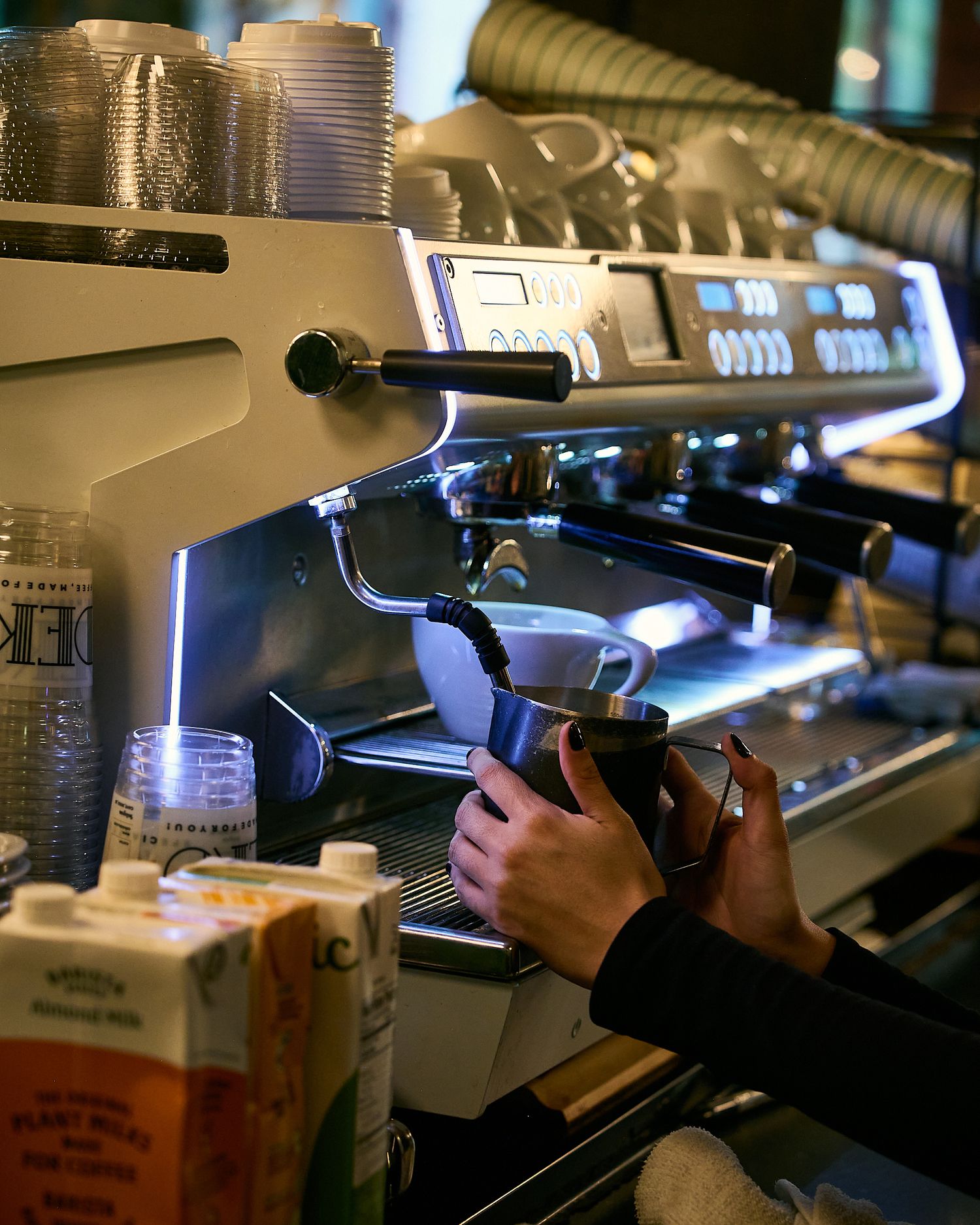 Barista steaming milk on a professional espresso machine with almond milk cartons nearby.
