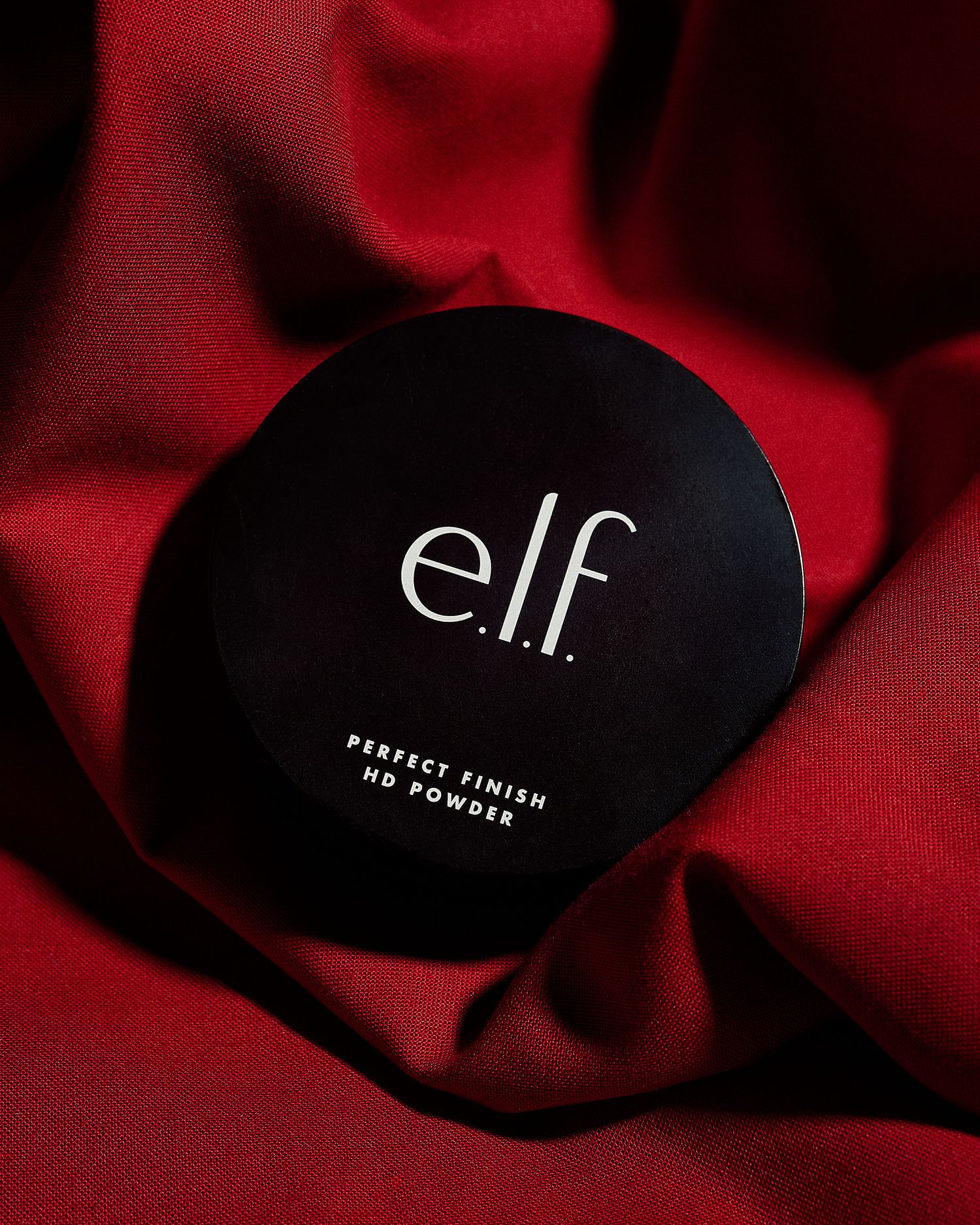 e.l.f. Perfect Finish HD Powder compact in black packaging resting on luxurious red satin fabric.
