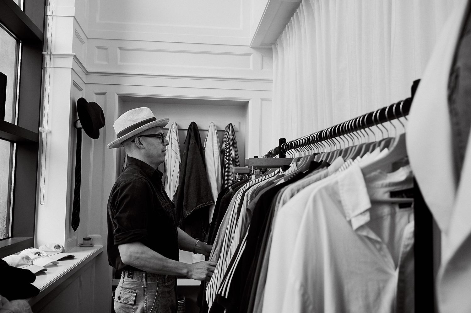 Man in hat browsing clothing rack in black and white boutique shop.