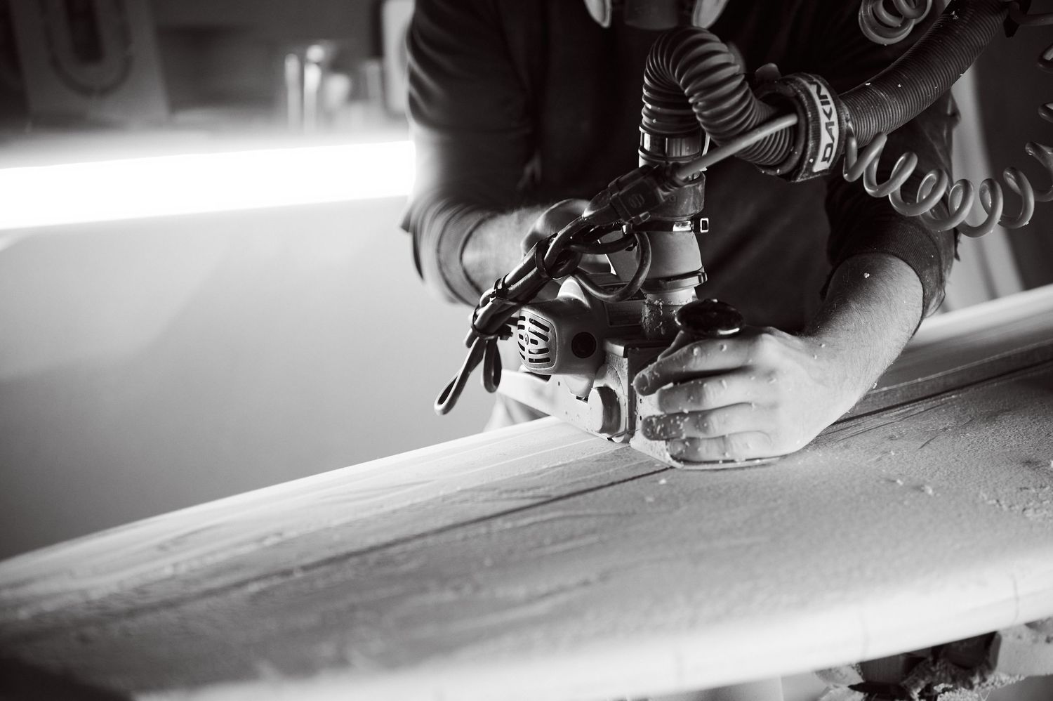 A craftsman uses a power planer to shape the rails of a surfboard blank.
