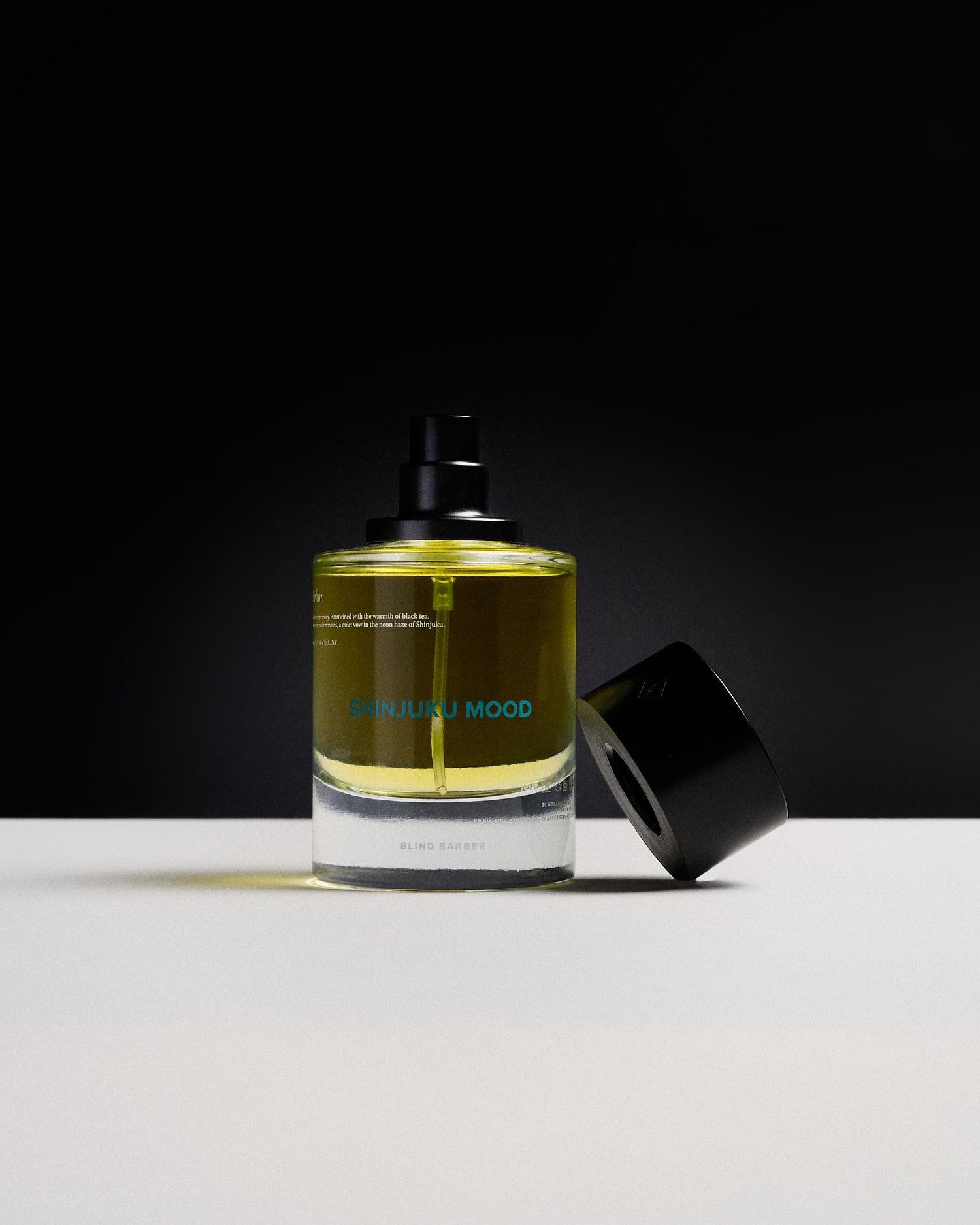 Luxury perfume bottle with olive-green liquid and black cap, labeled MOOD, displayed on white surface against dark background.