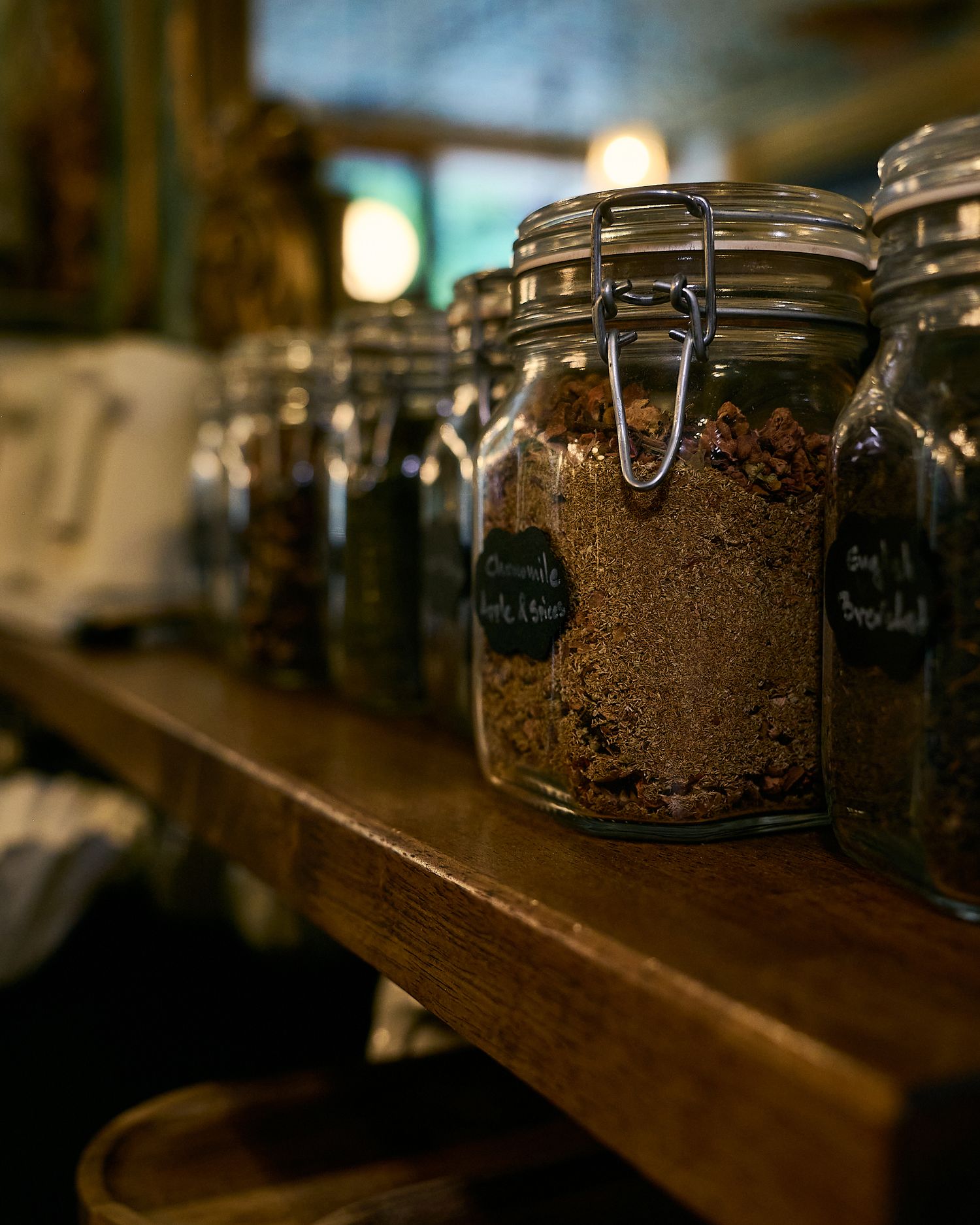 Glass jars filled with spices and herbs displayed on a rustic wooden shelf in warm ambient lighting.