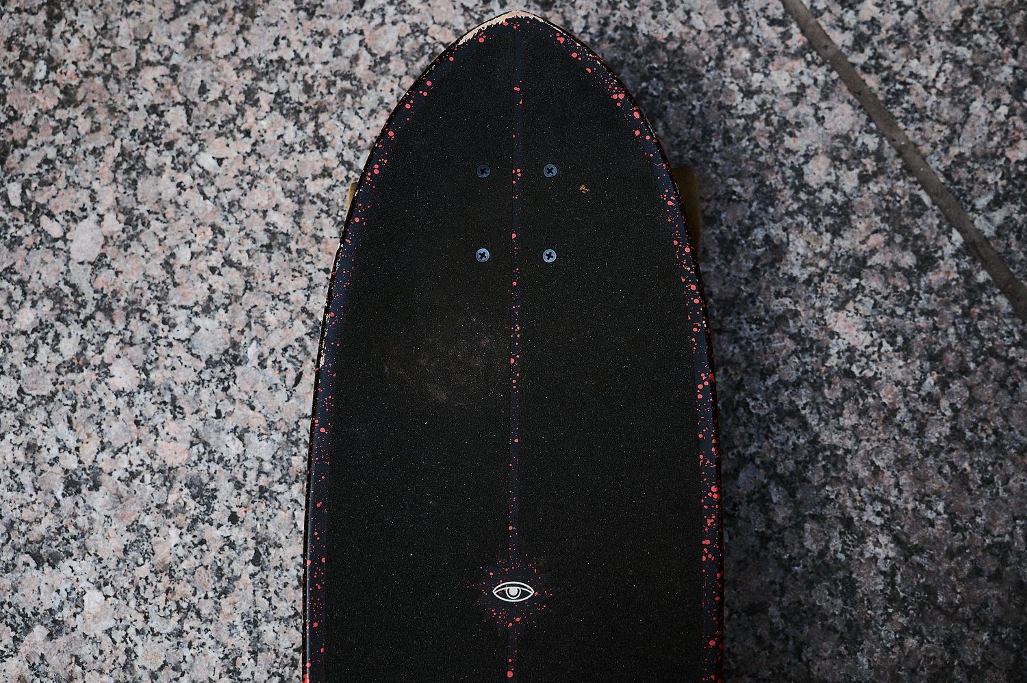 Close-up of a black skateboard deck with red trim on a granite surface.