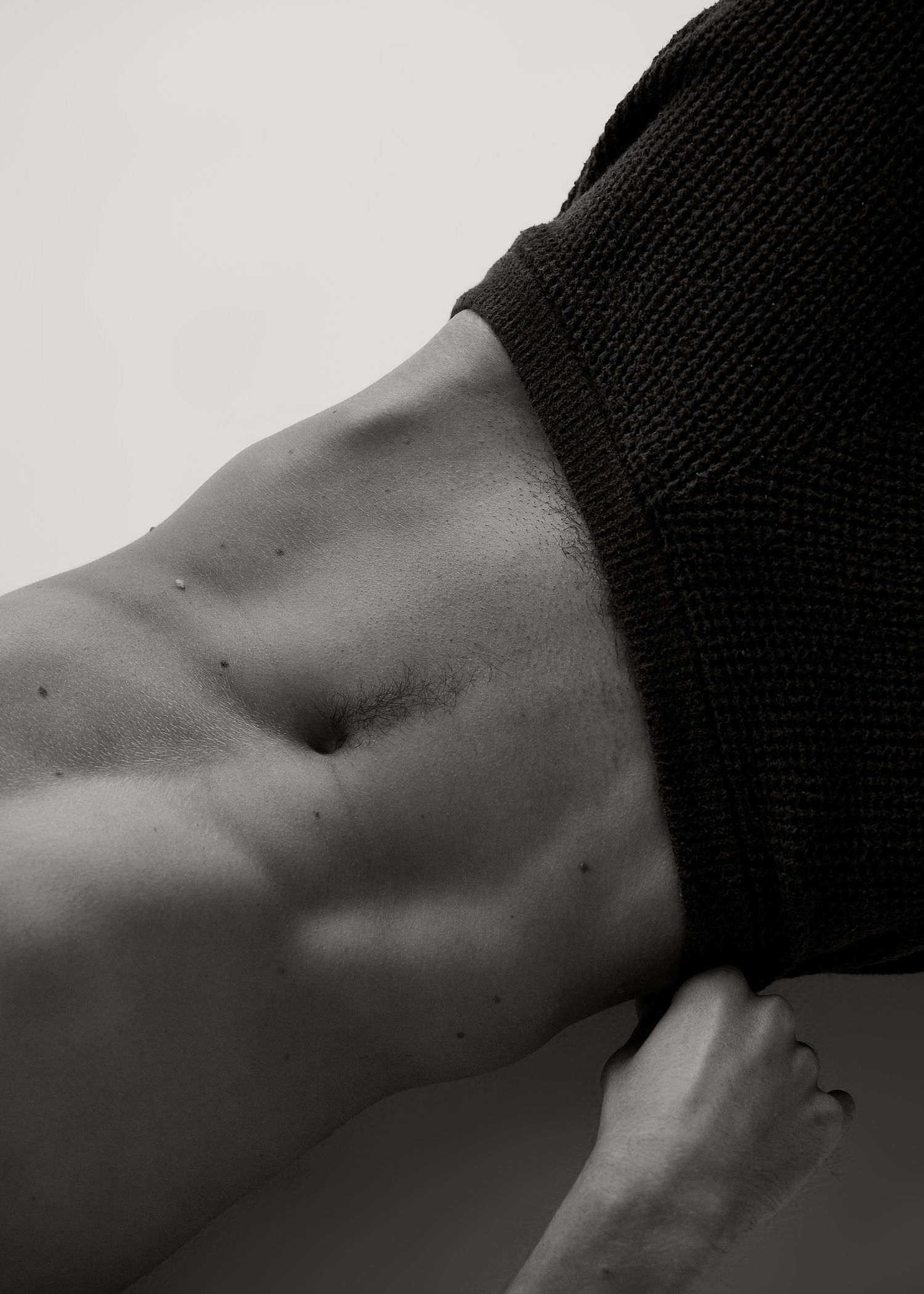 Black and white close-up of a fit person's toned abs and midsection with a dark sweater lifted up.