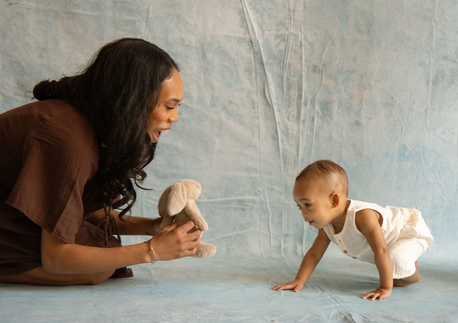 A mother plays with her crawling baby using a stuffed toy during a professional photo session.