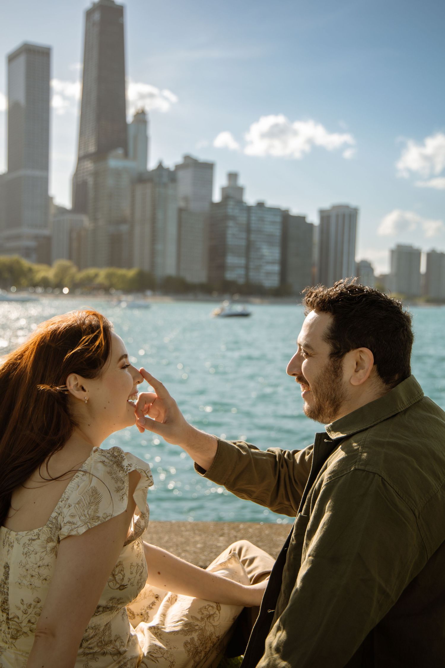 Laughing couple sitting together by Lake Michigan with the Chicago skyline behind them.