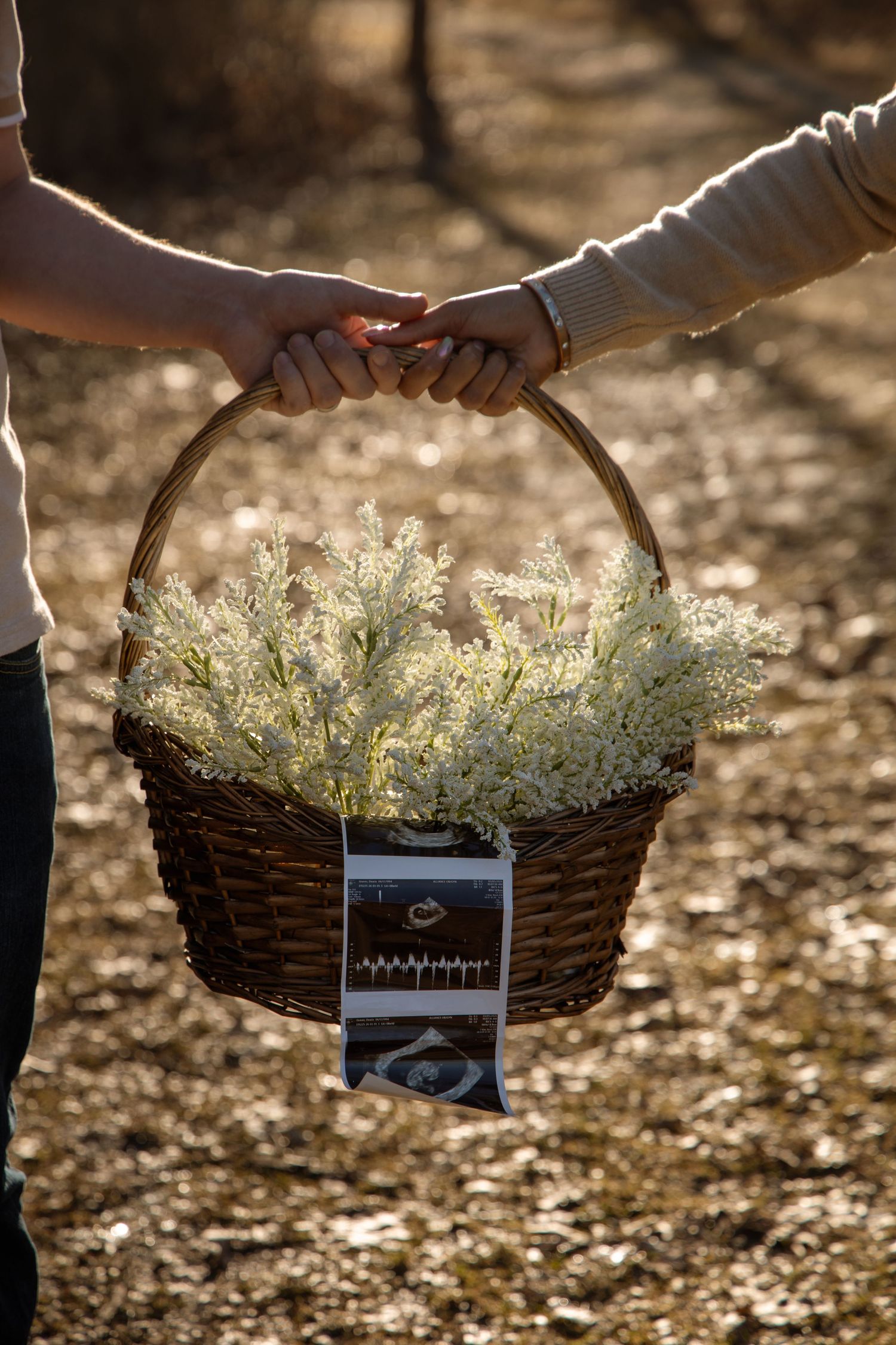 Two people holding a wicker basket with white flowers and ultrasound photos attached.