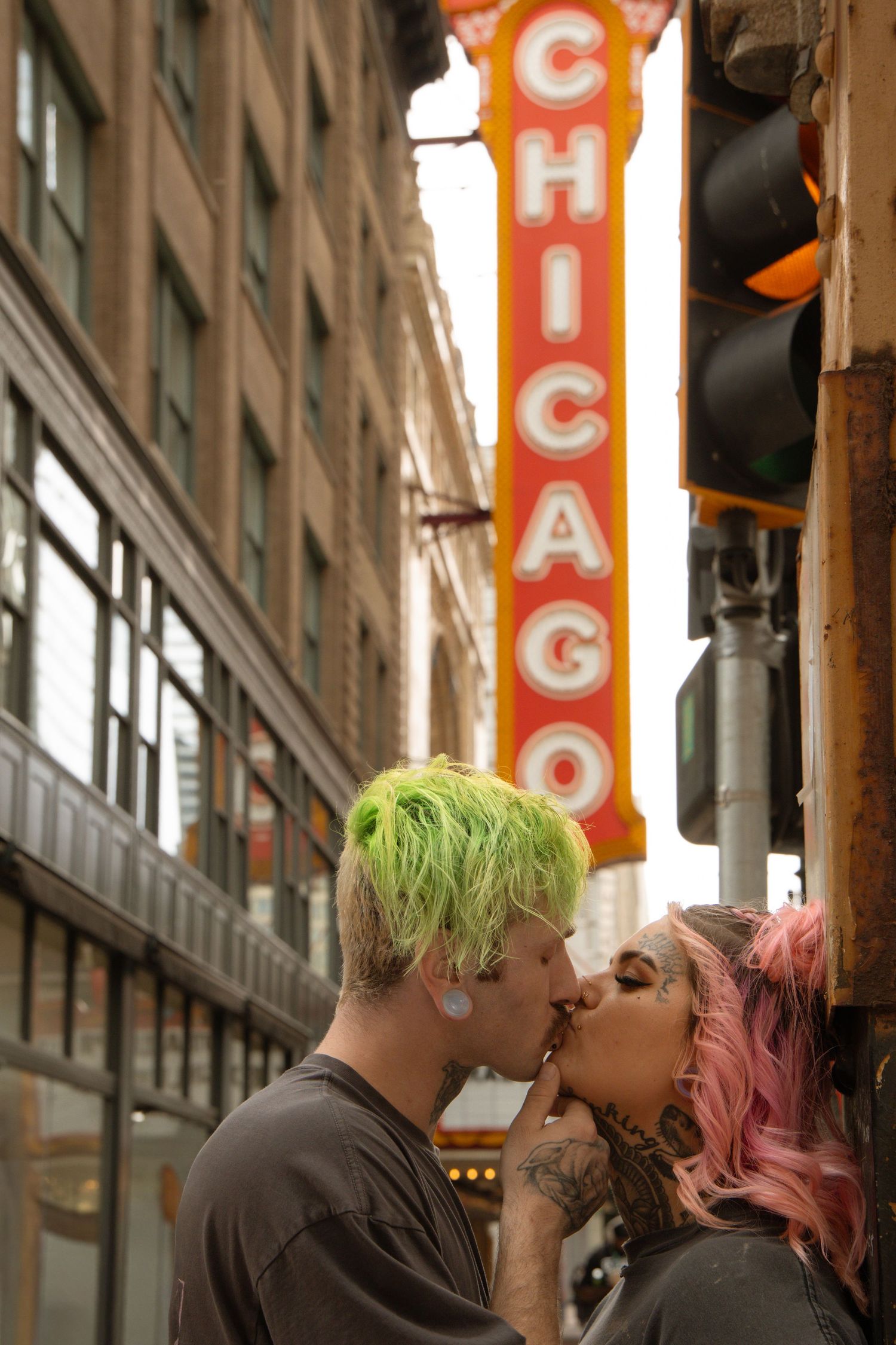 Couple with colorful hair kissing on a Chicago street beneath the iconic Chicago Theatre marquee sign.