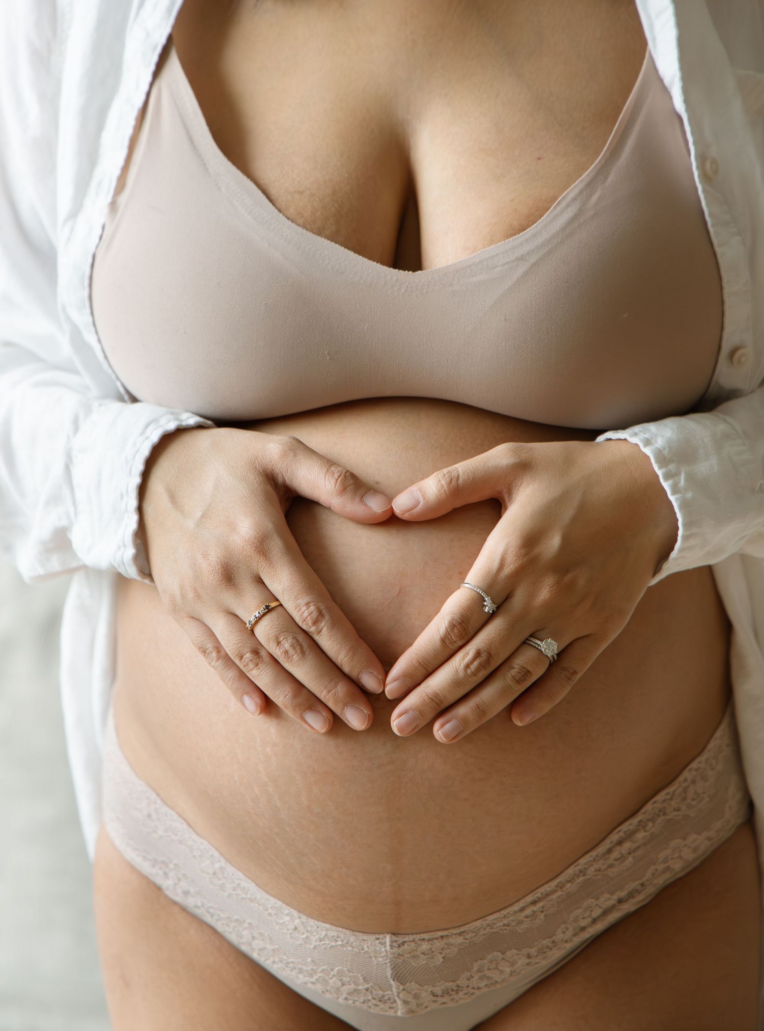 Pregnant woman in white bra and underwear forming heart shape with hands on baby bump.