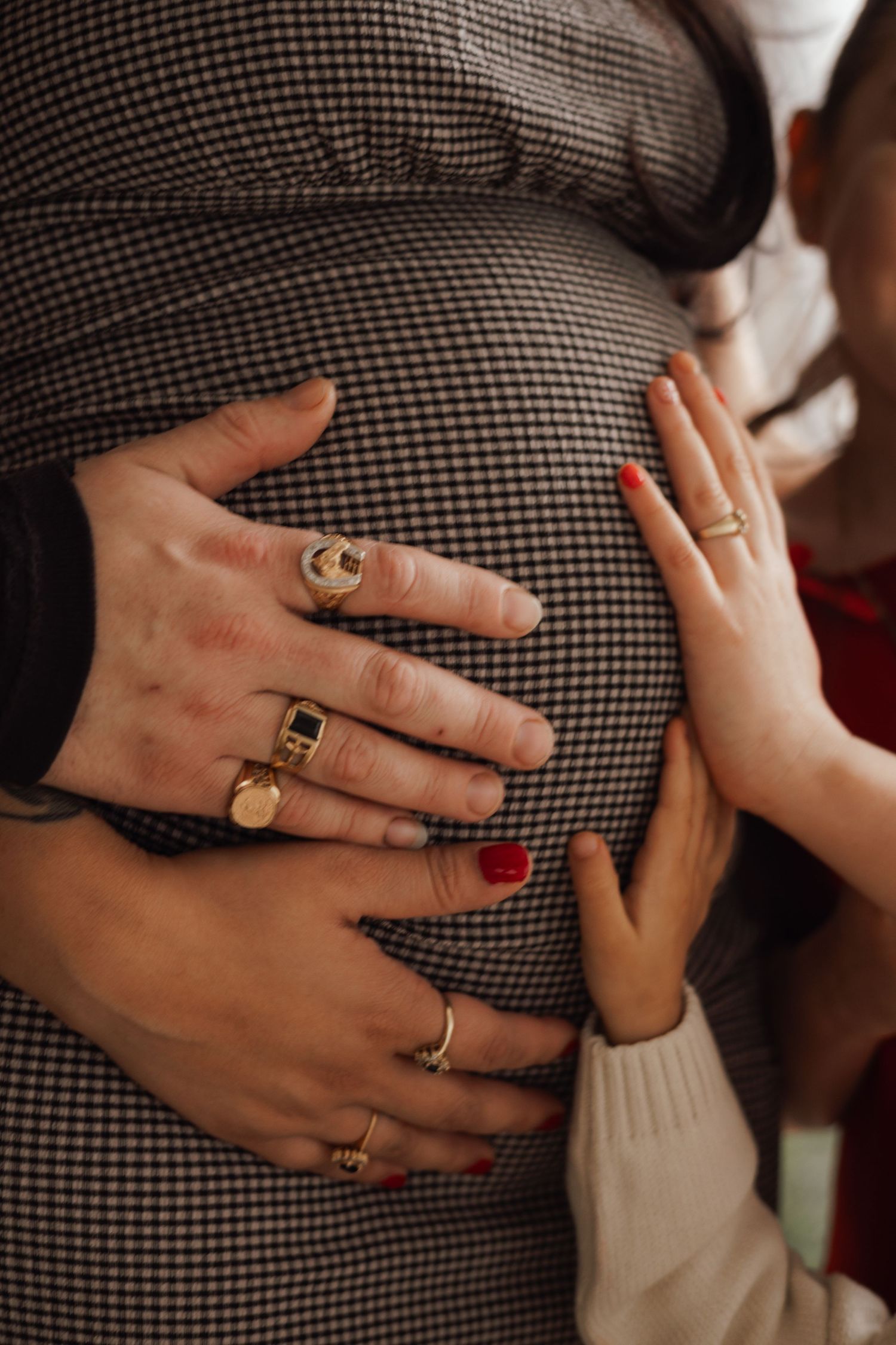 Close-up of hands with gold rings resting on a pregnant belly in a checkered dress.