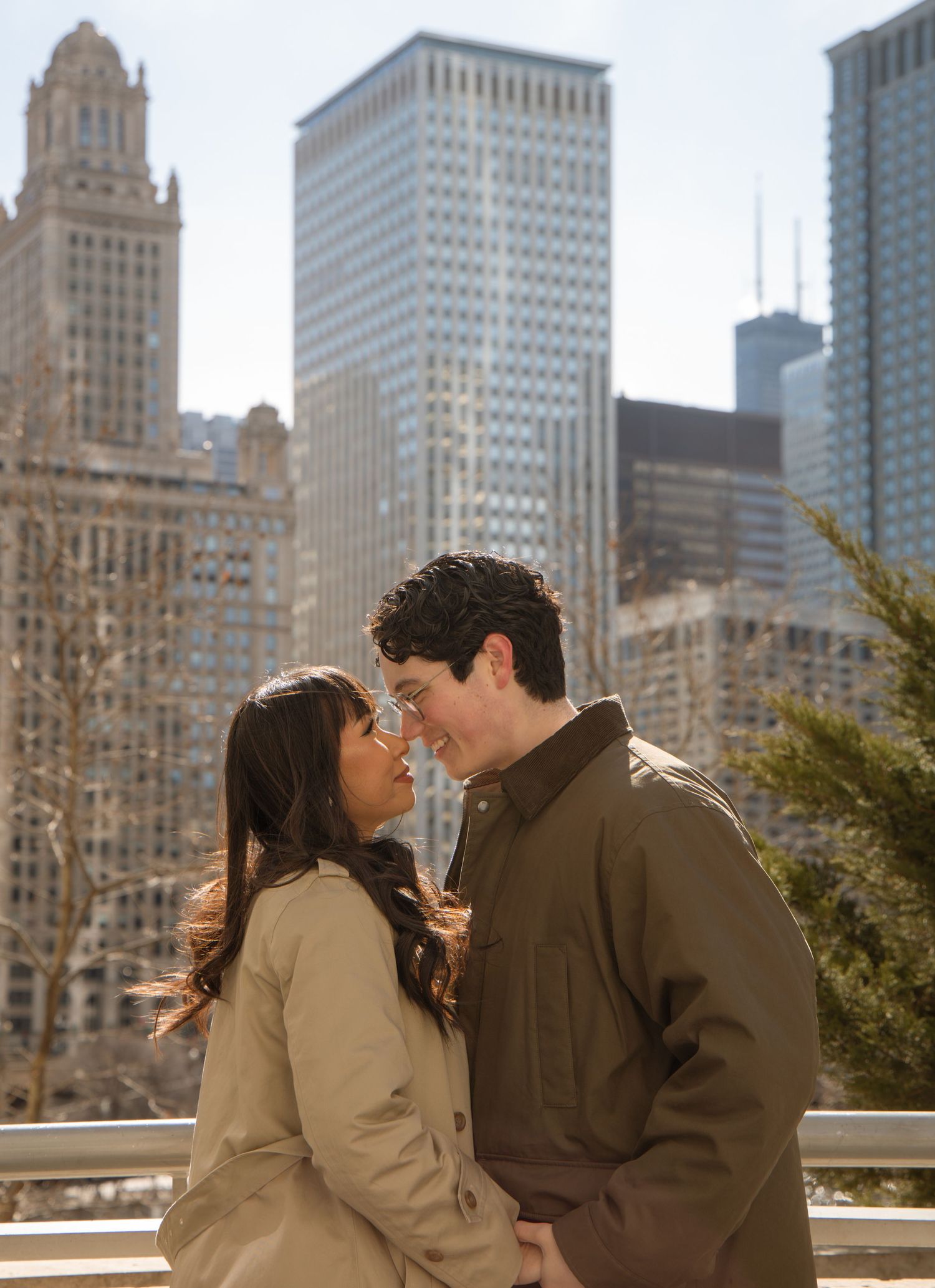 Couple leans in for a kiss with Chicago skyscrapers and blue sky in background.