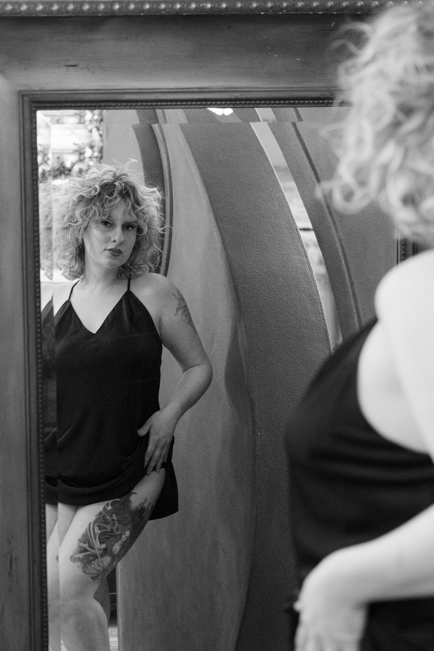 Black and white photo of tattooed woman reflected in ornate vintage mirror.
