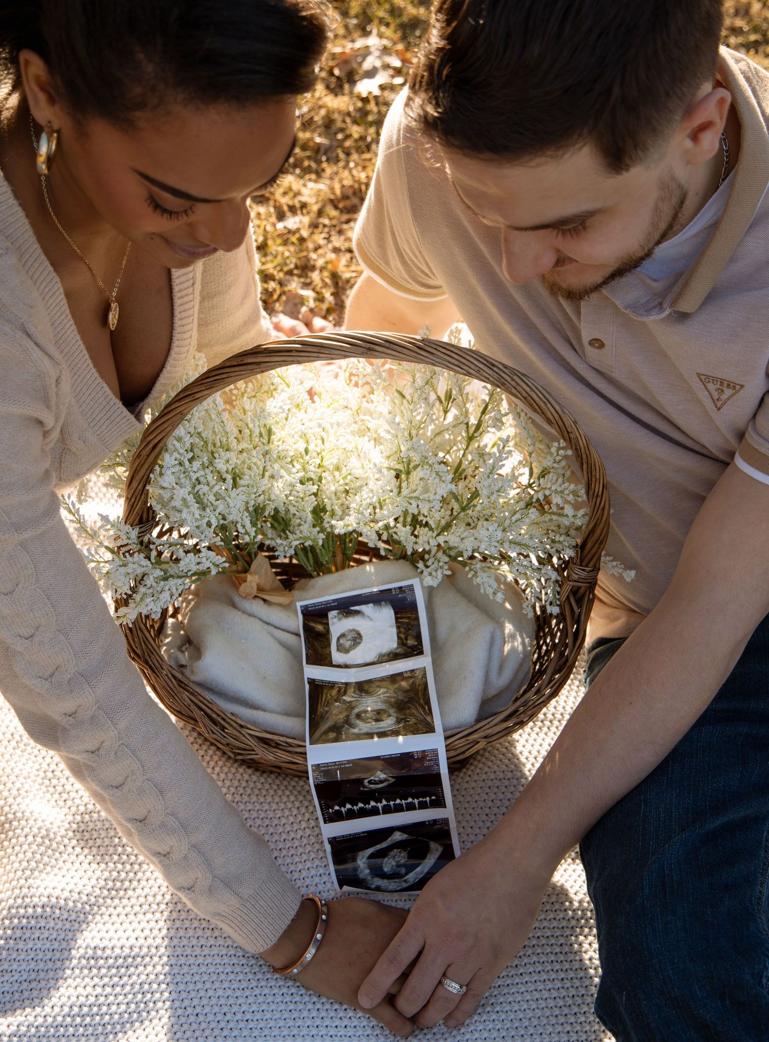 Couple looking down at ultrasound photos inside a wicker basket filled with white flowers.