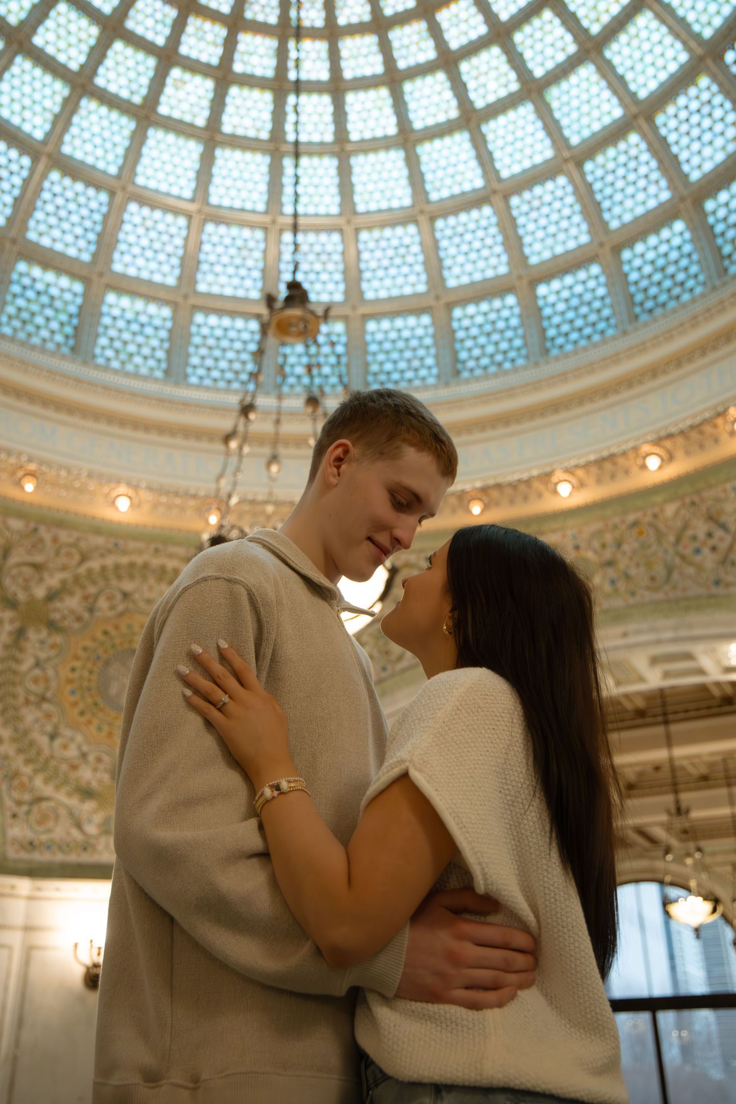 Romantic couple embracing under a stunning ornate stained glass dome ceiling in a grand building.