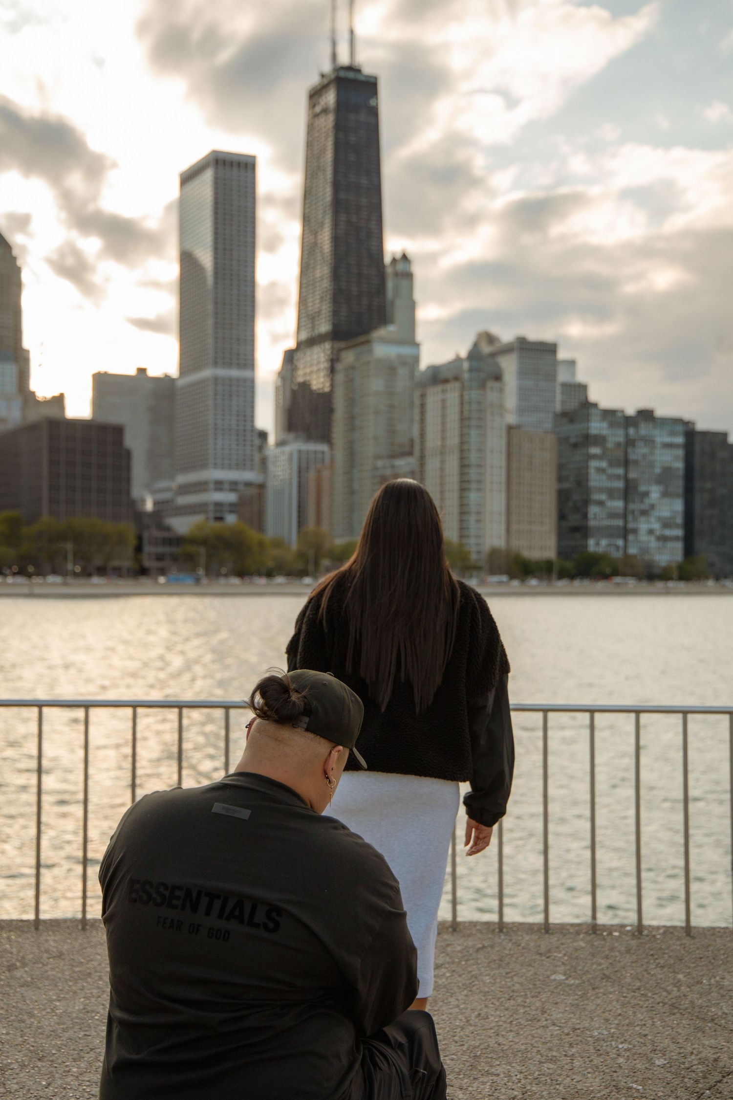 Photographer crouching with a light reflector while a woman poses by a railing with the Chicago skyline at sunset.