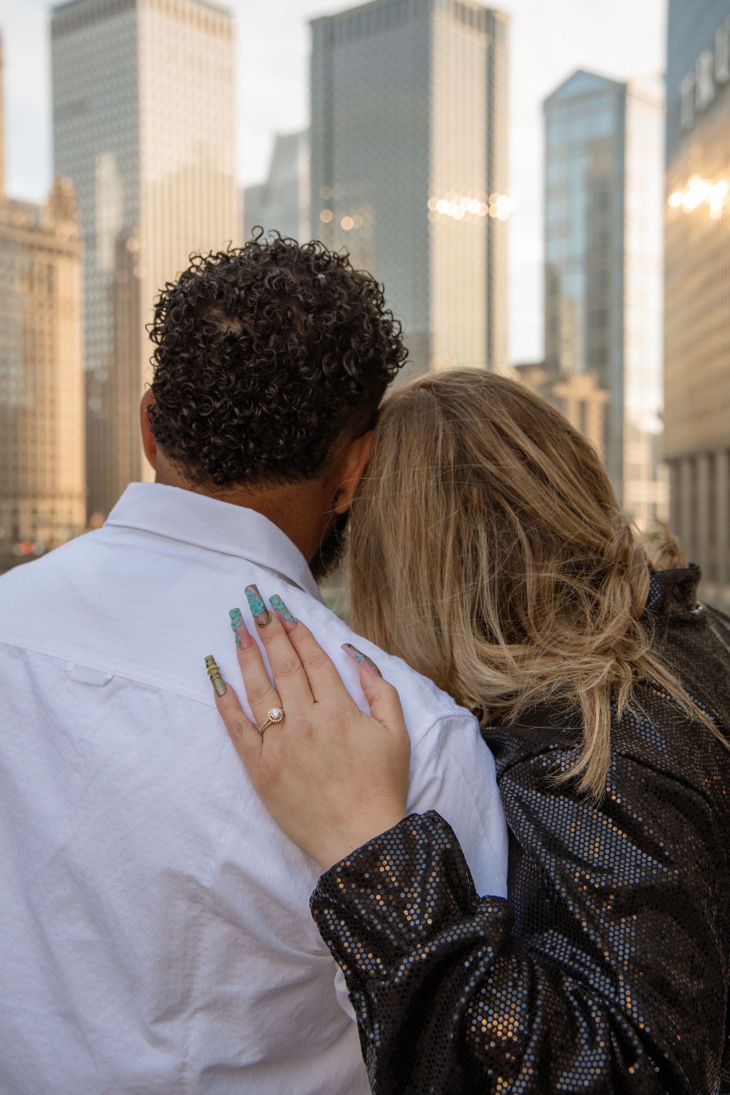 Newly engaged couple gazes at Chicago skyline, woman displaying ring on mans shoulder.