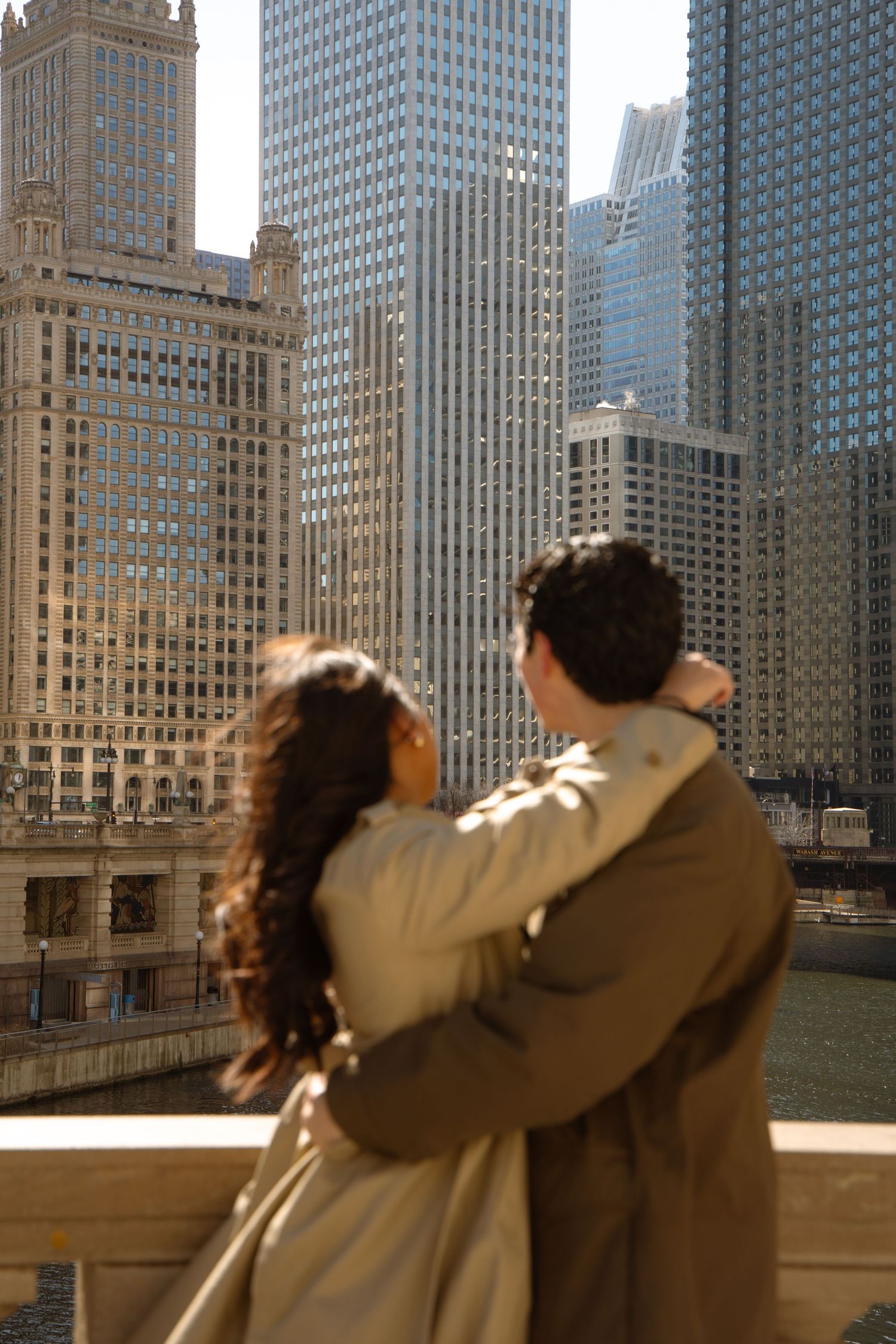 Couple hugs while admiring the Chicago River skyline from a decorative bridge railing.