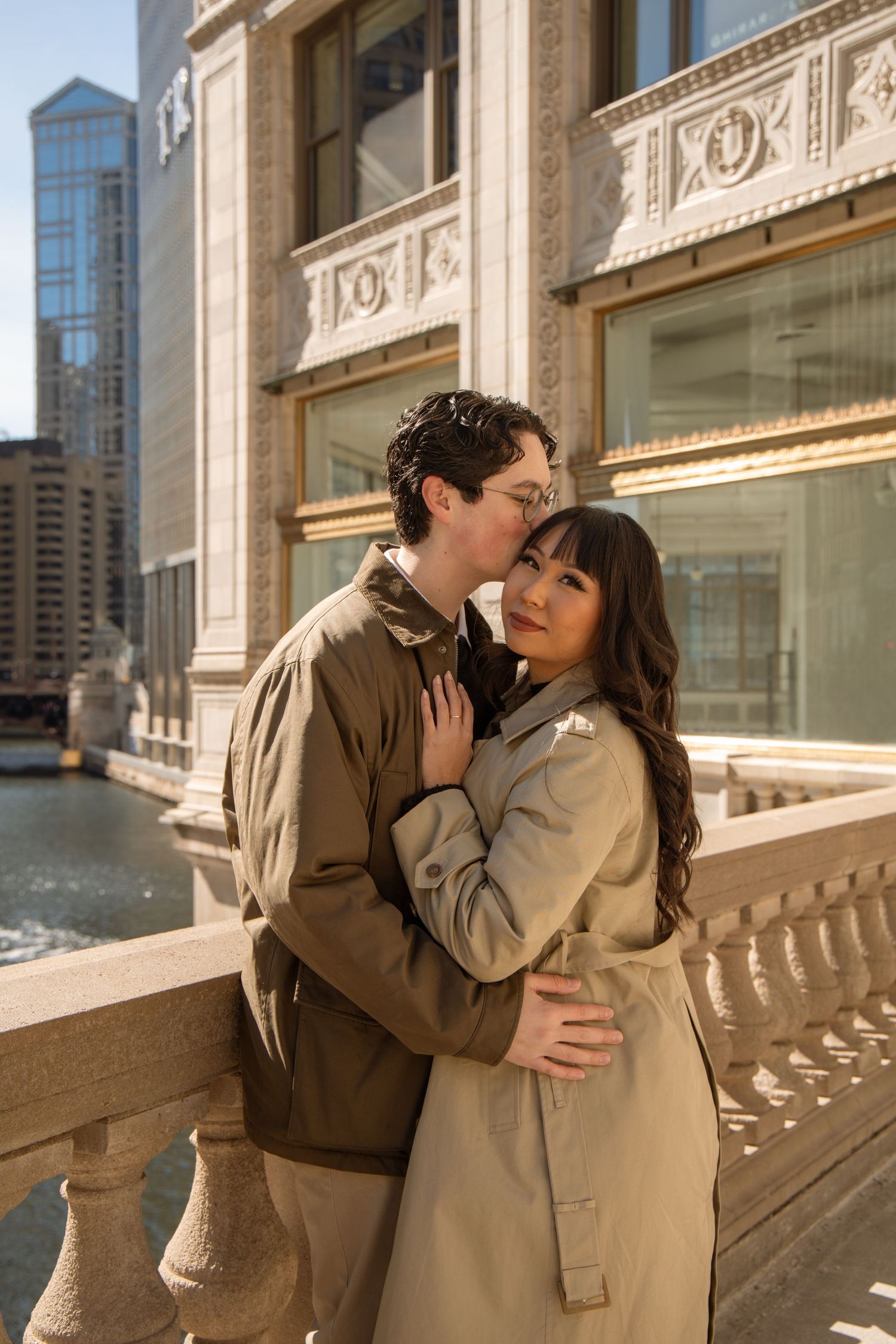 Couple embraces tenderly on a ornate bridge with Chicago River and buildings behind them.