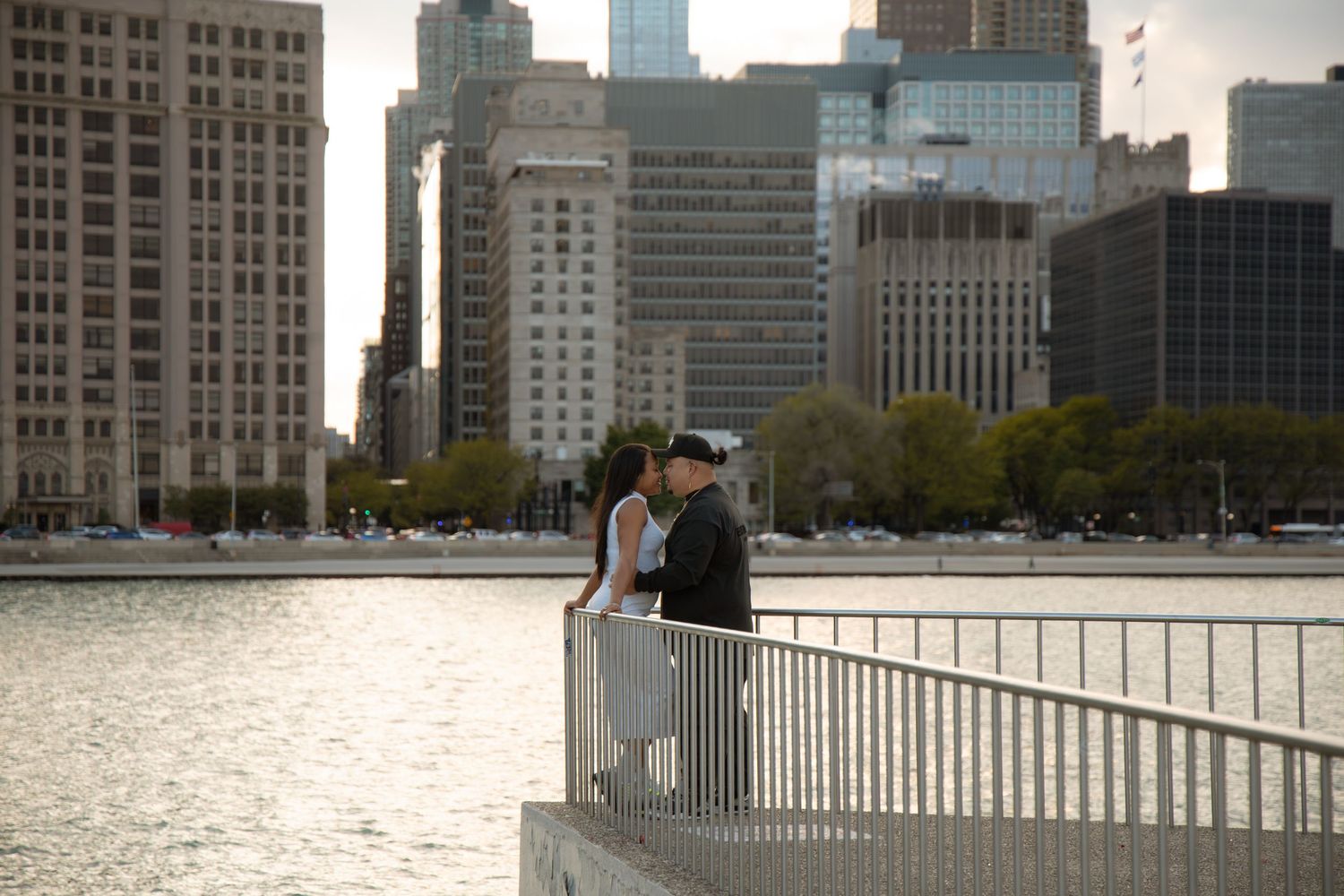 Couple sharing a romantic moment on a waterfront railing with Chicago city skyline in the background.