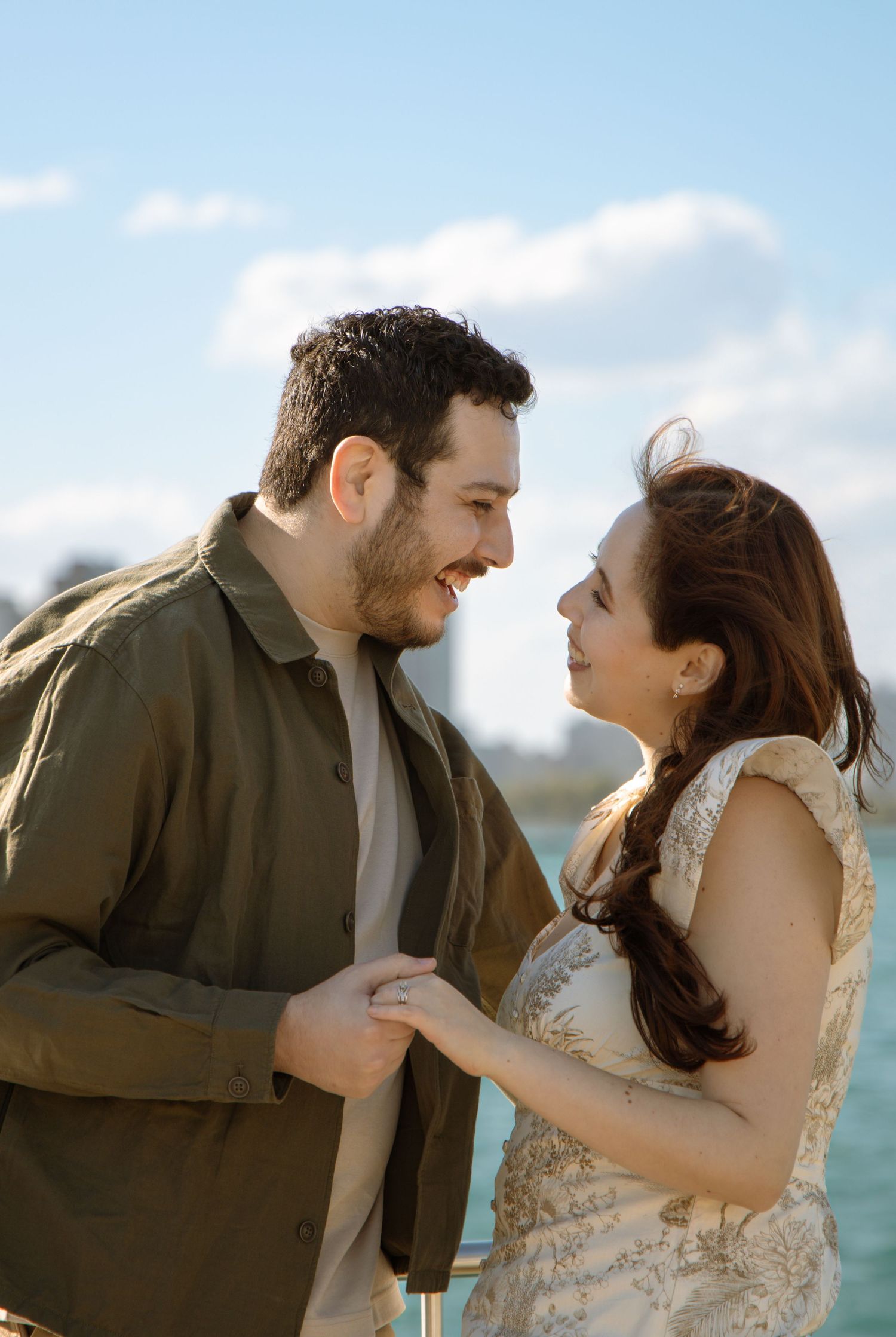 Couple sharing a romantic moment holding hands outdoors near water under a bright blue sky.