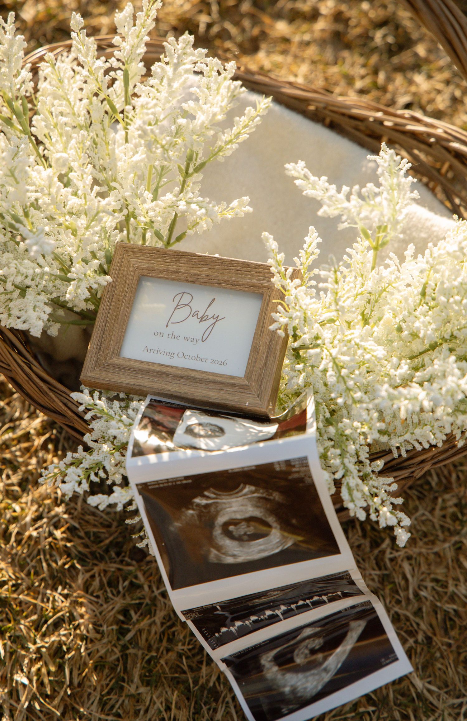 Baby announcement display with ultrasound photos, a framed sign, and white flowers in a basket.