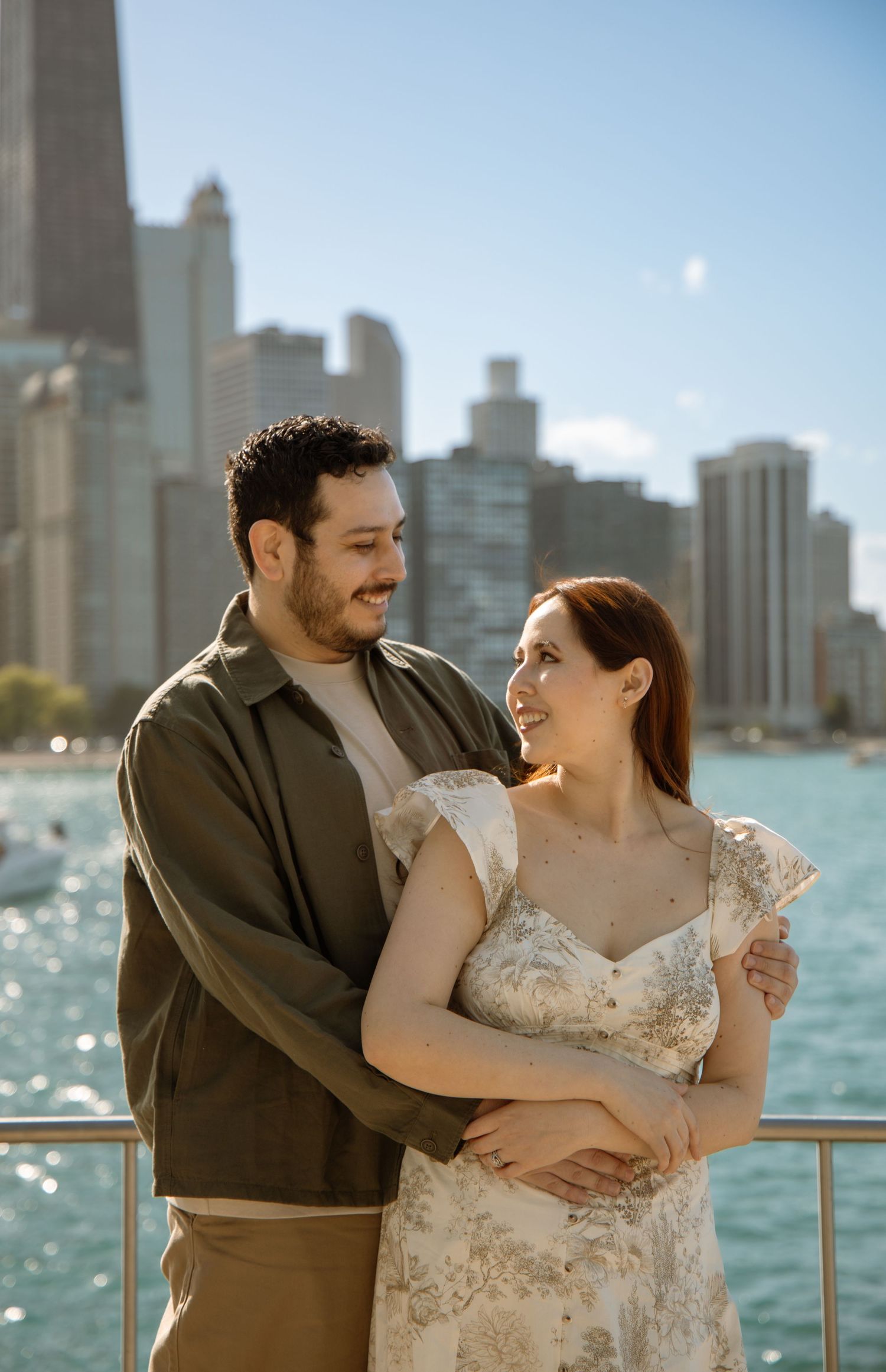 Couple embracing and smiling with Chicago skyline and lake in background on a sunny day.