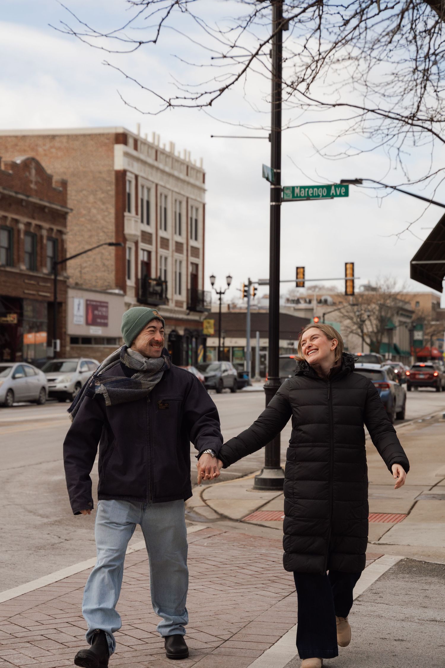 Happy couple holding hands and laughing while walking on brick sidewalk at Marengo Ave intersection.
