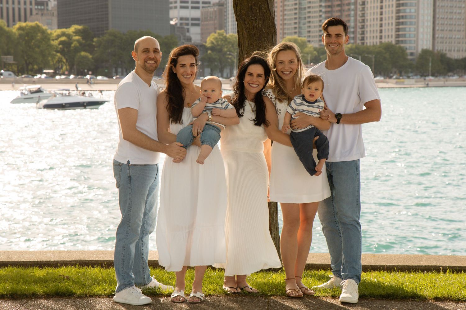 Family group photo with two babies outdoors near a waterfront on a sunny day.