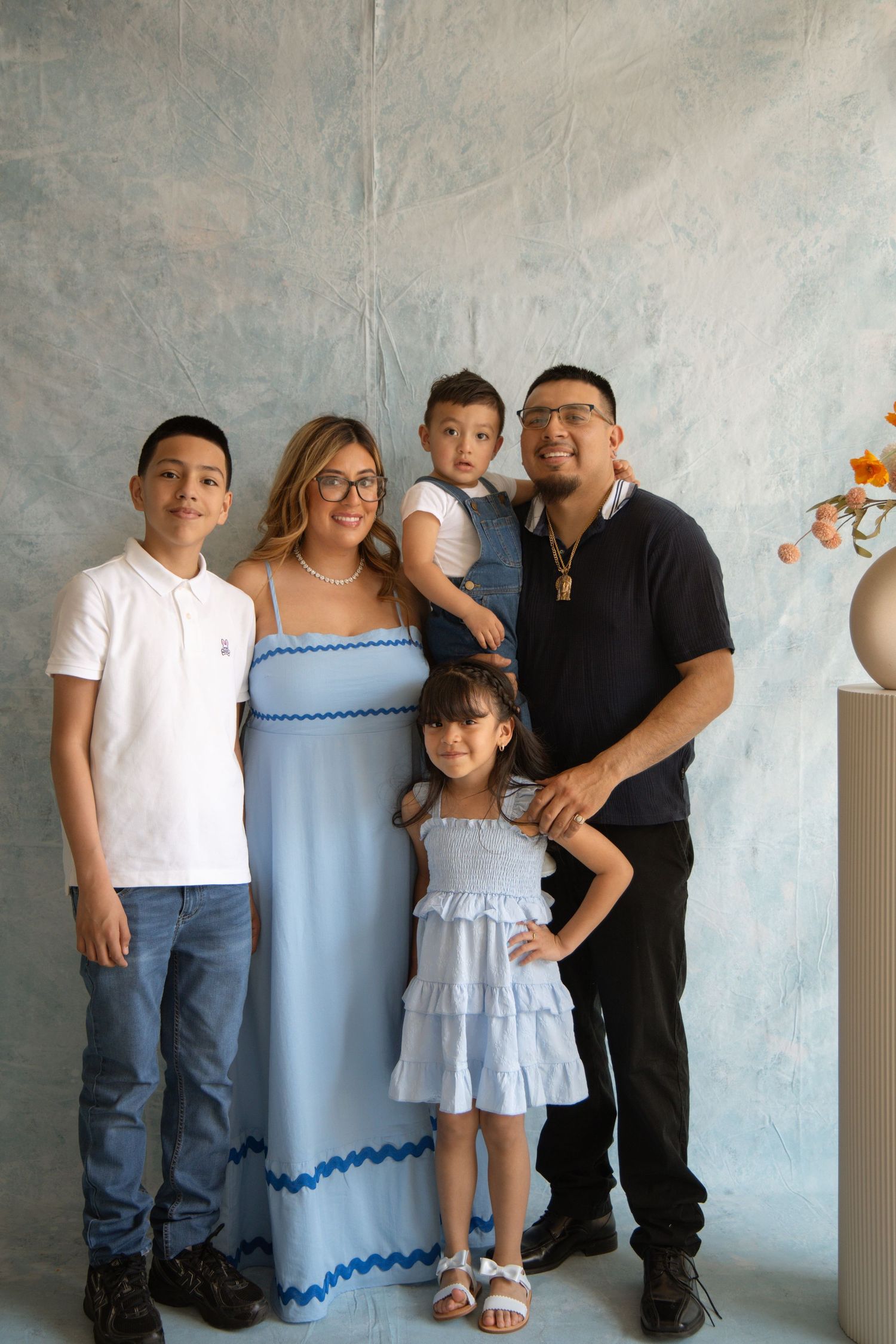 Family of five posing for a portrait, parents with two boys and a girl, dressed in coordinating blue and white outfits.