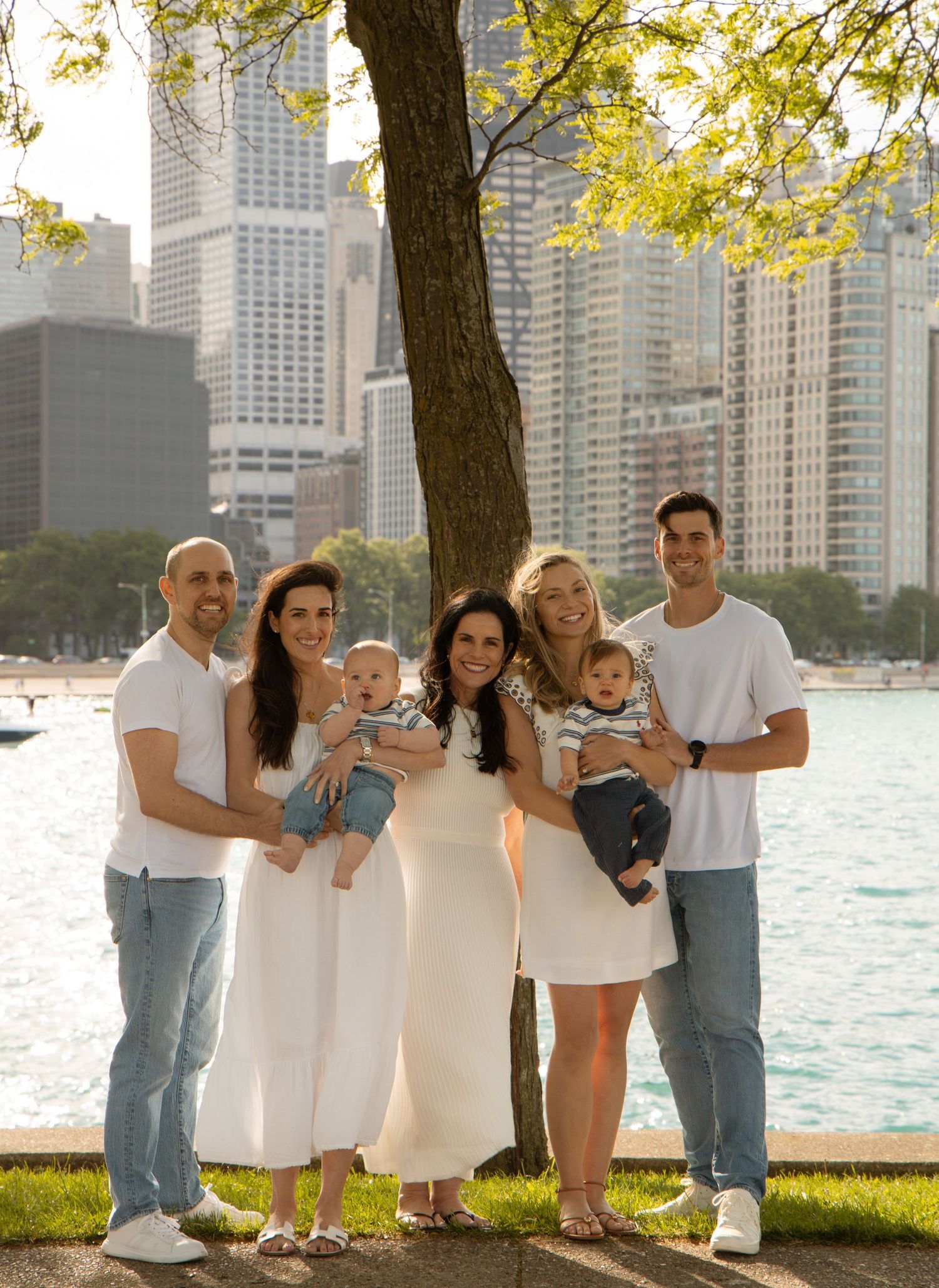 Family of seven posing in white outfits by a lakeside park with Chicago city skyline in the background.