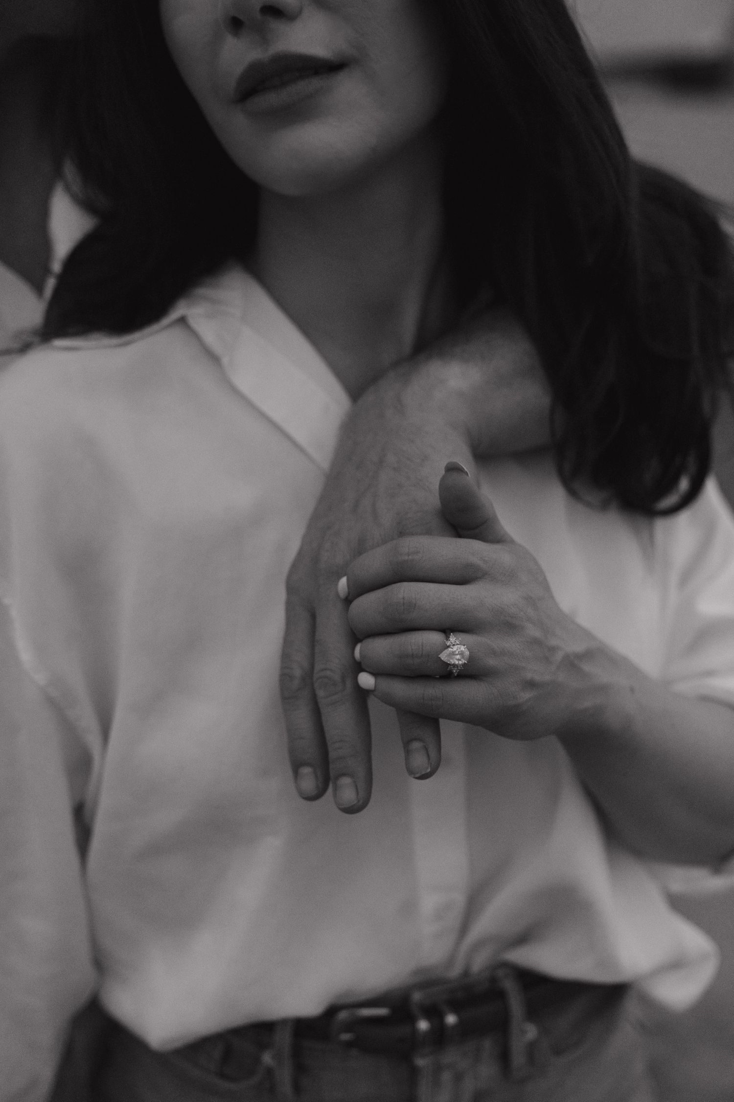Black and white photo of a woman in white shirt displaying an engagement ring on her finger.