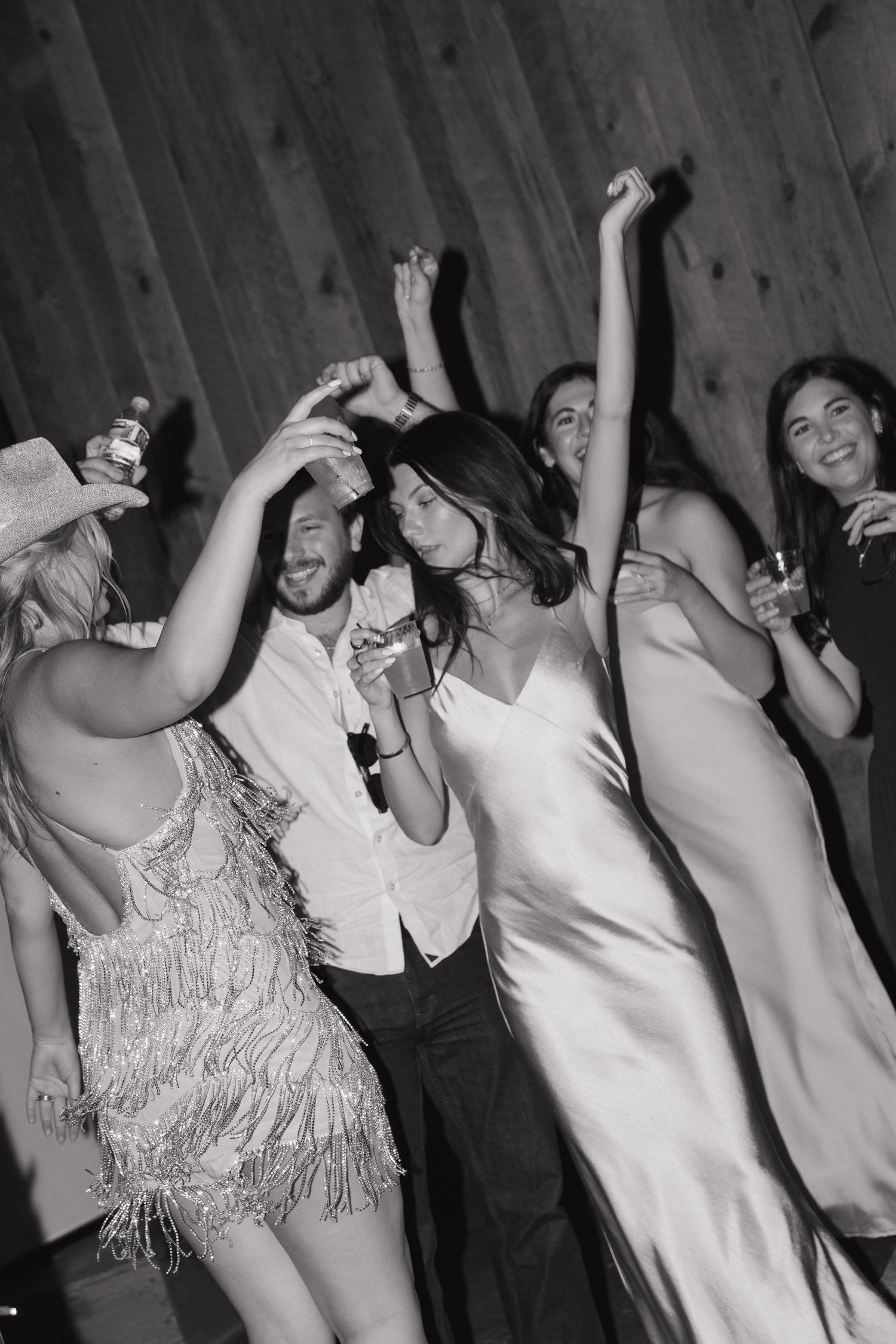Black and white photo of bride groom and guests dancing joyfully at wedding reception.