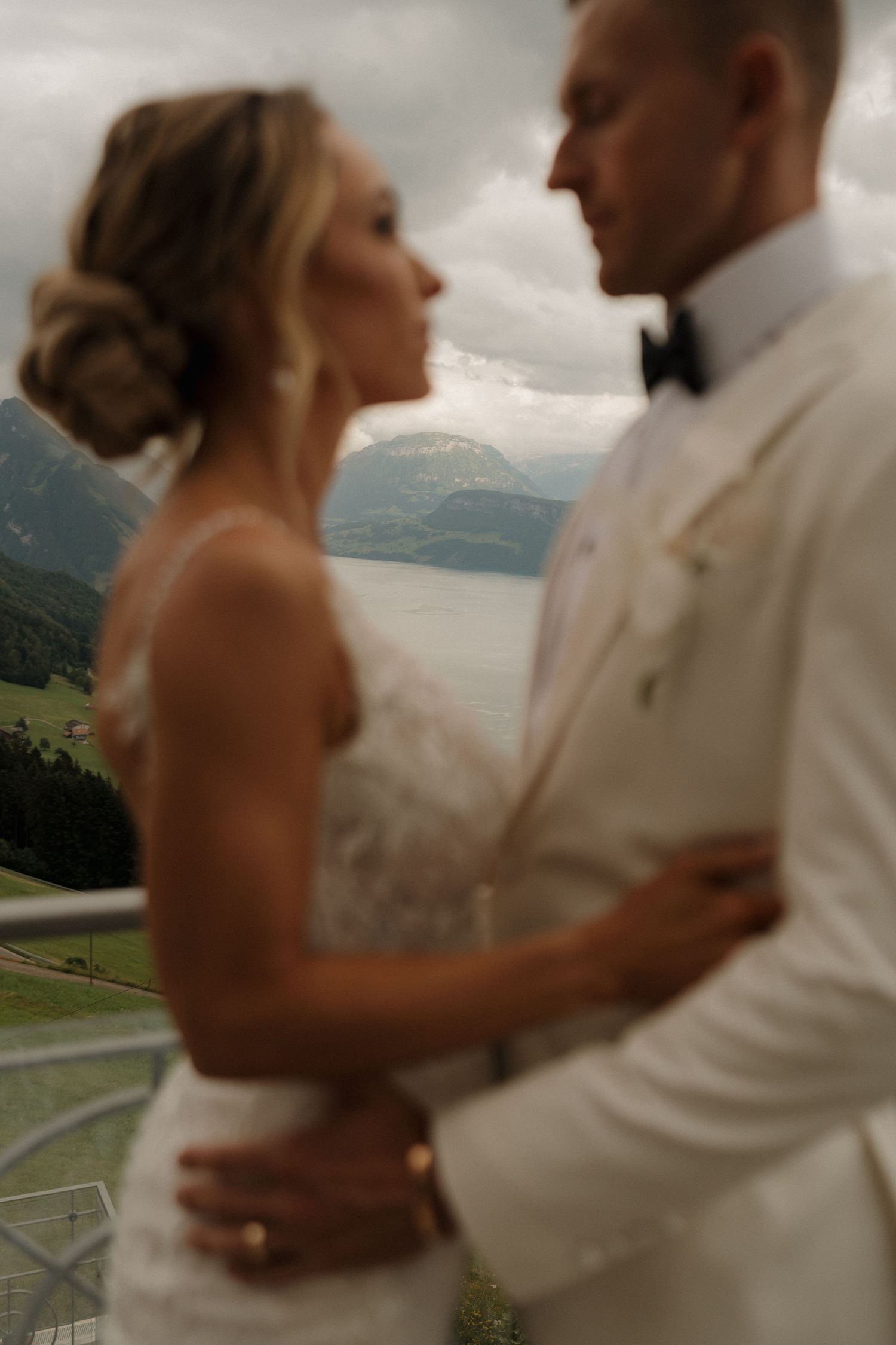 Soft focus close-up of bride and groom gazing at each other on balcony with Swiss lake mountain backdrop.