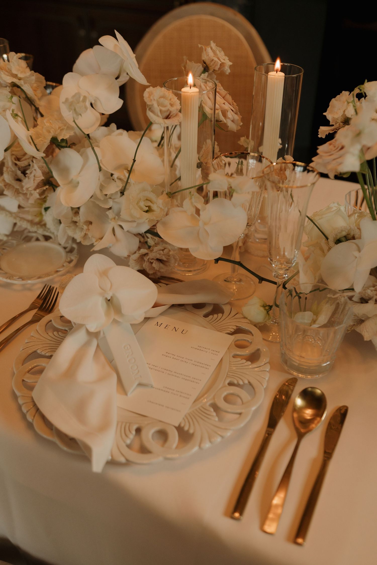 Elegant wedding place setting with white orchid, menu card, gold cutlery, and ornate decorative plate.