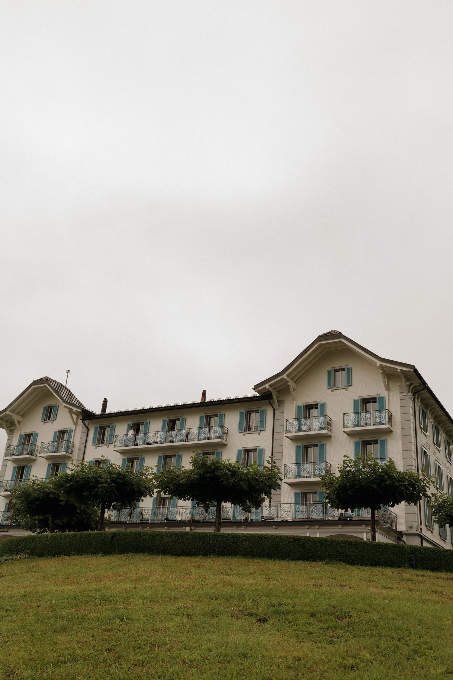 Elegant white European hotel building with balconies and trees on a cloudy day.