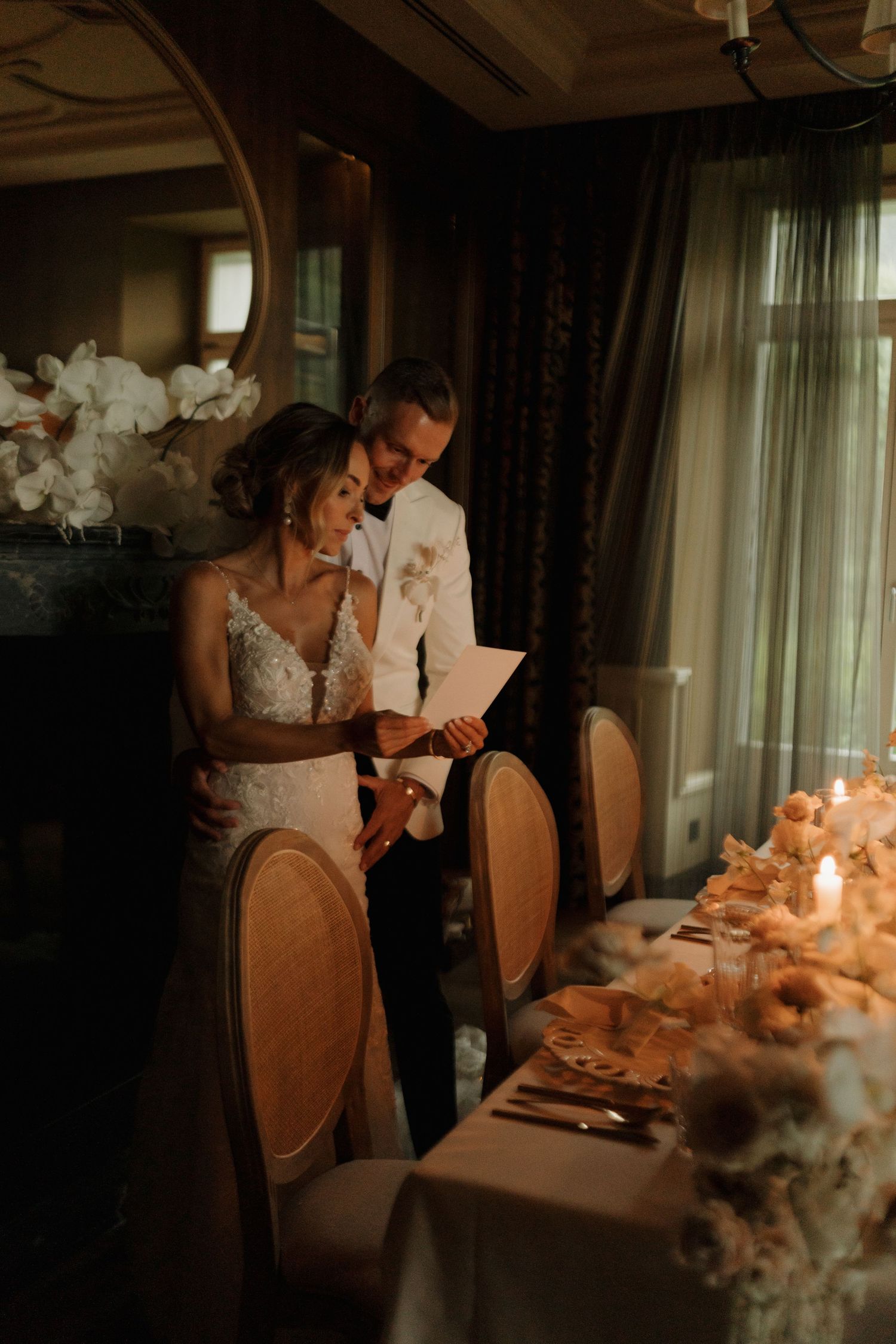 Bride and groom read menu card together beside elegantly decorated candlelit wedding reception dinner table.