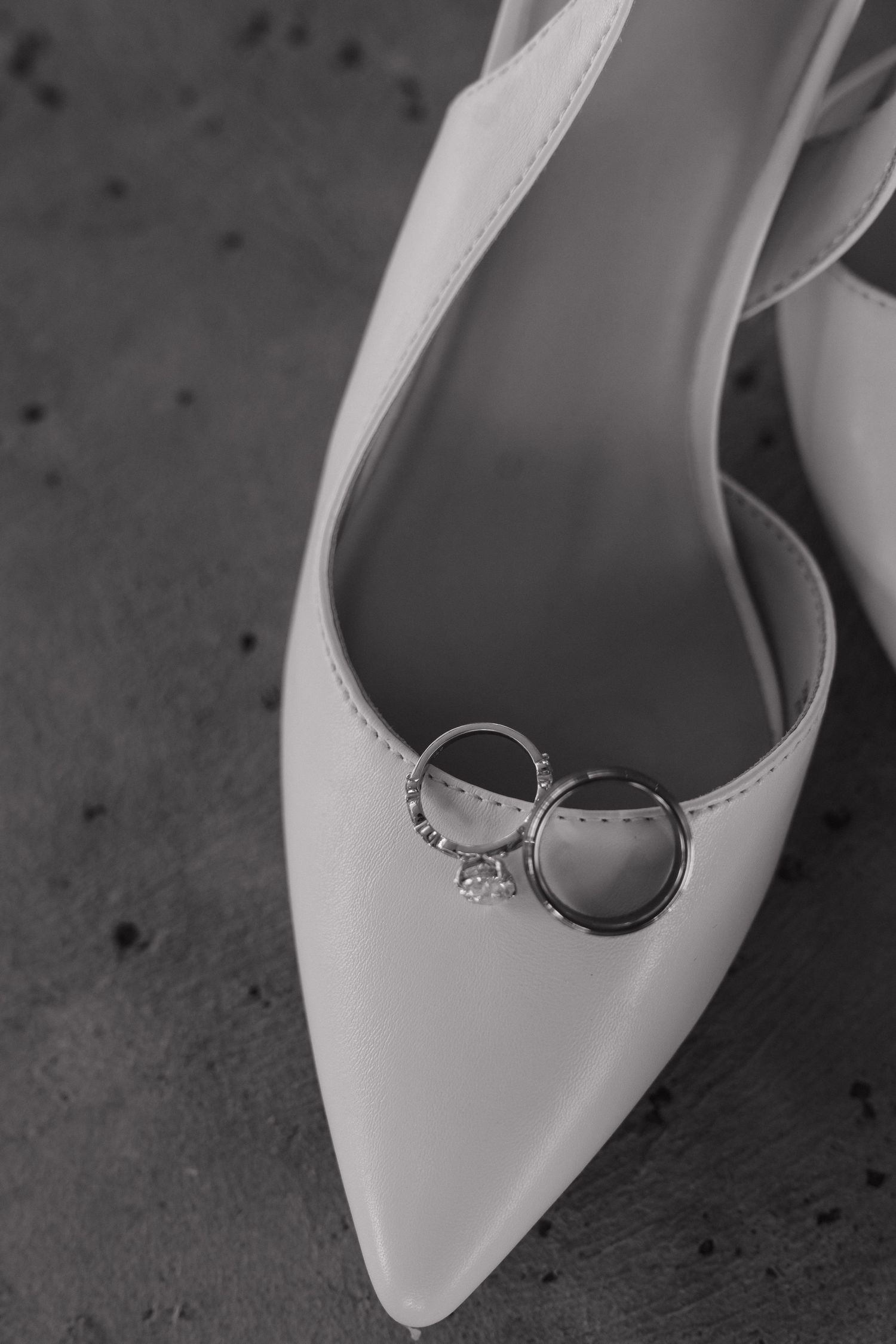Black and white close-up of diamond engagement ring and wedding band resting on white bridal heels.