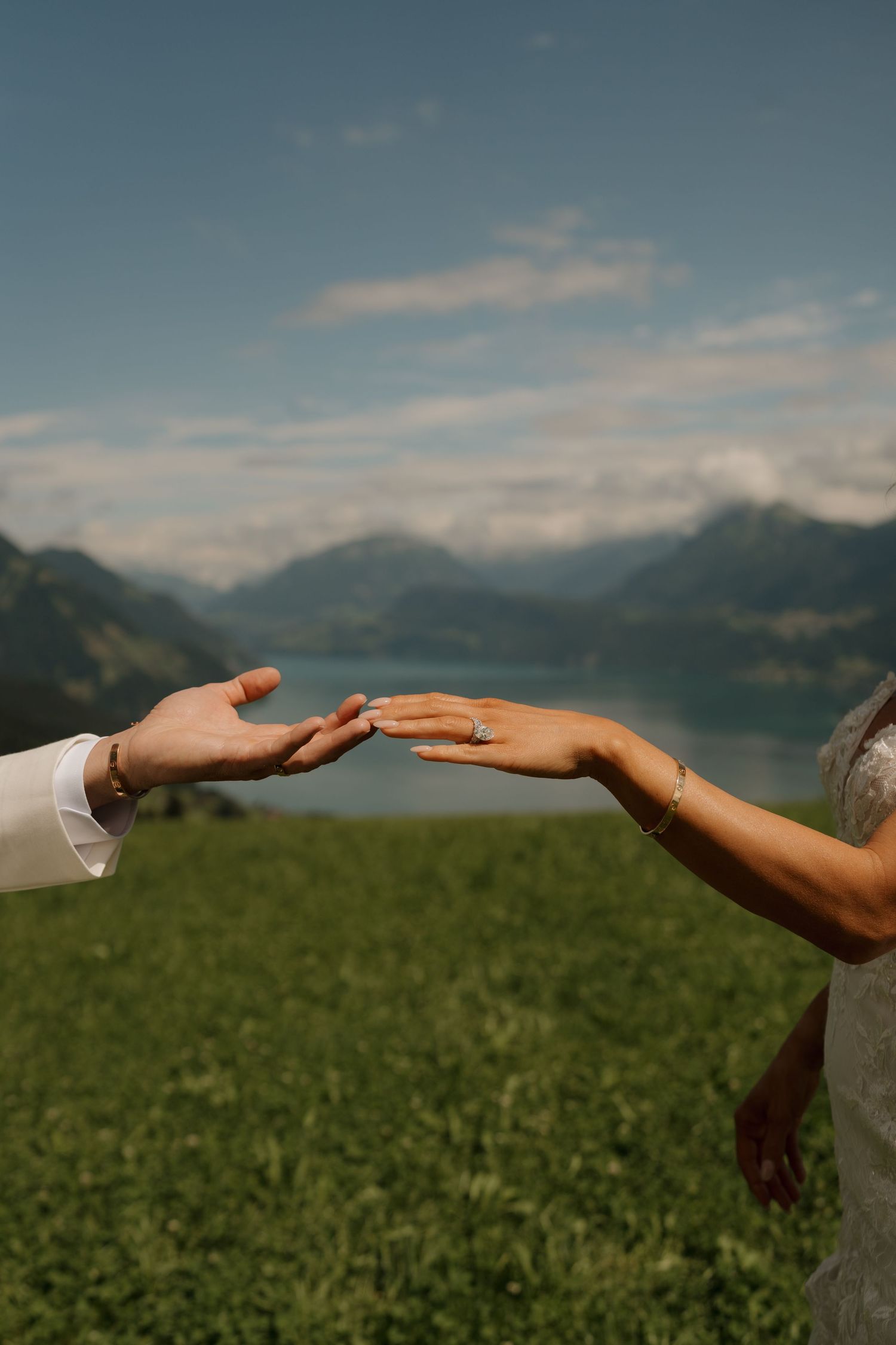 Bride and groom reaching toward each other with alpine lake and mountain backdrop on wedding day.